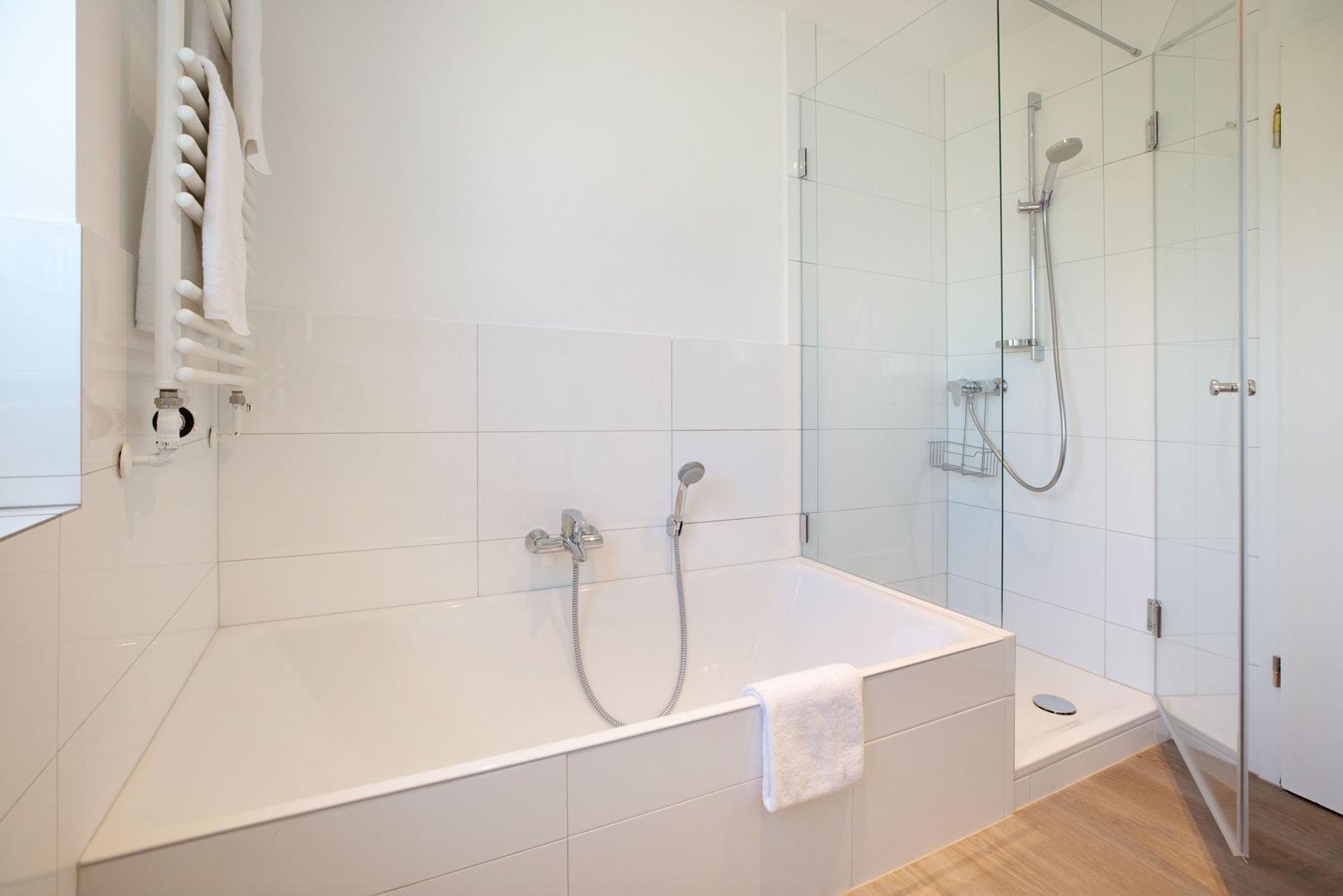 Bad mit Badewanne und Dusche, weiß gefliest, Handtuchhalter und Handtuch.