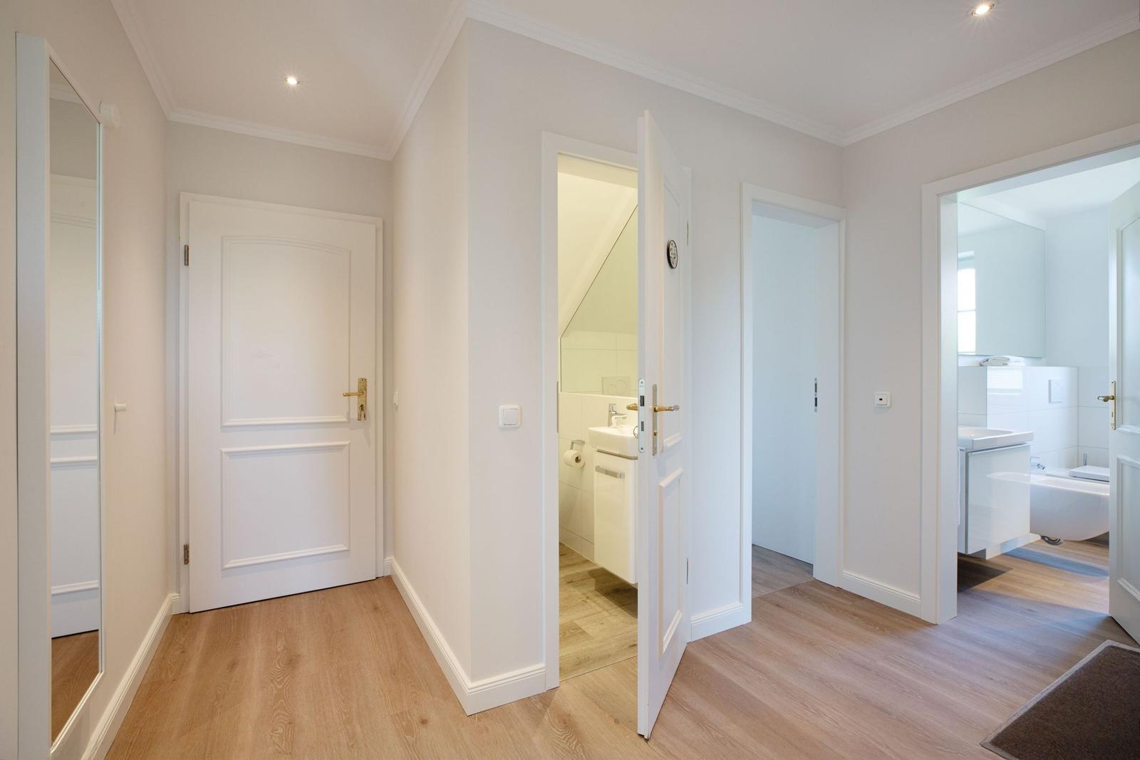 Flur mit Tür zu Bad und Schlafzimmer, Holzboden und weiße Türen.