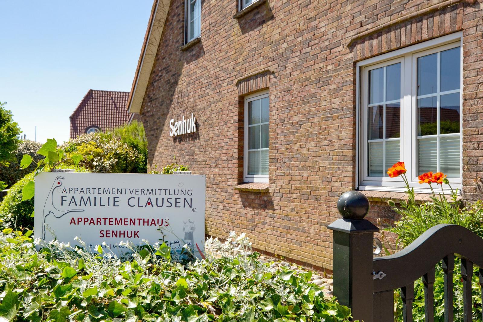 Ferienhaus Senhuk mit Schild und Blumenbeet vor Backsteinfassade