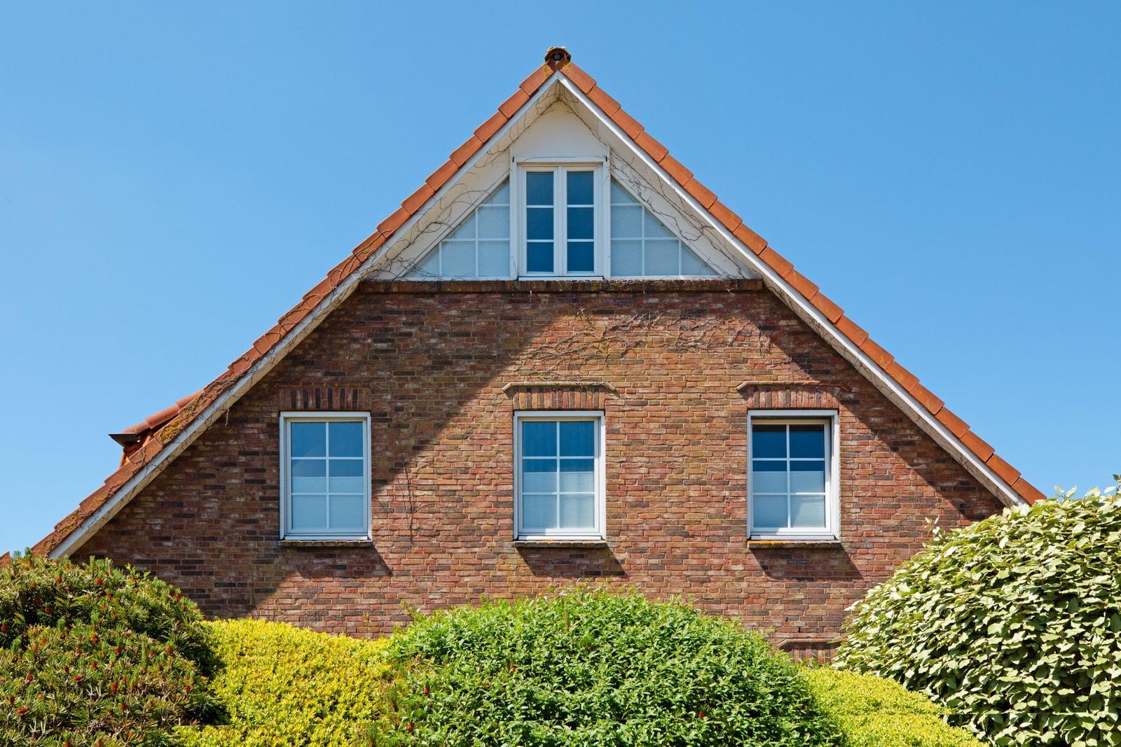 Rotes Ziegelhaus mit Dachfenster und weißen Fenstern. Grünhecken im Vordergrund.