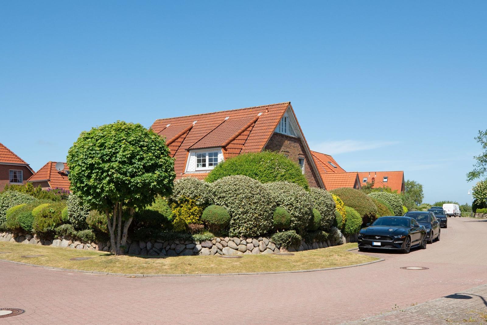 Haus mit rotem Dach, gepflegtem Garten und gepflastertem Weg. Mehrere Autos parken vor dem Haus.