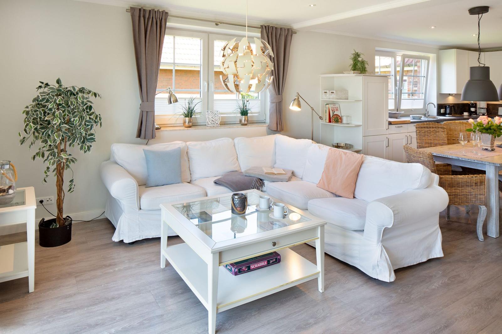 Wohnzimmer mit weißem Sofa, Glas-Tisch und Küchenbereich im Hintergrund.