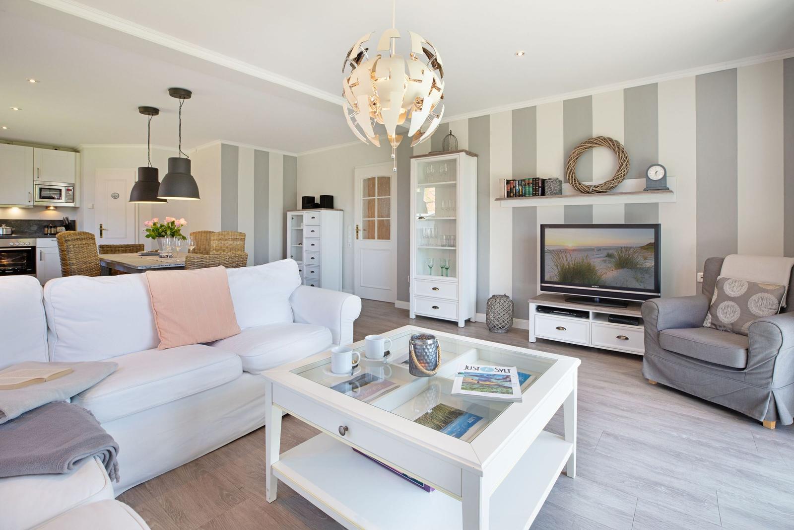 Wohnzimmer mit Sofa, Sessel und Glas-Tisch. Wand mit Streifen. Fernseher und Sideboard.