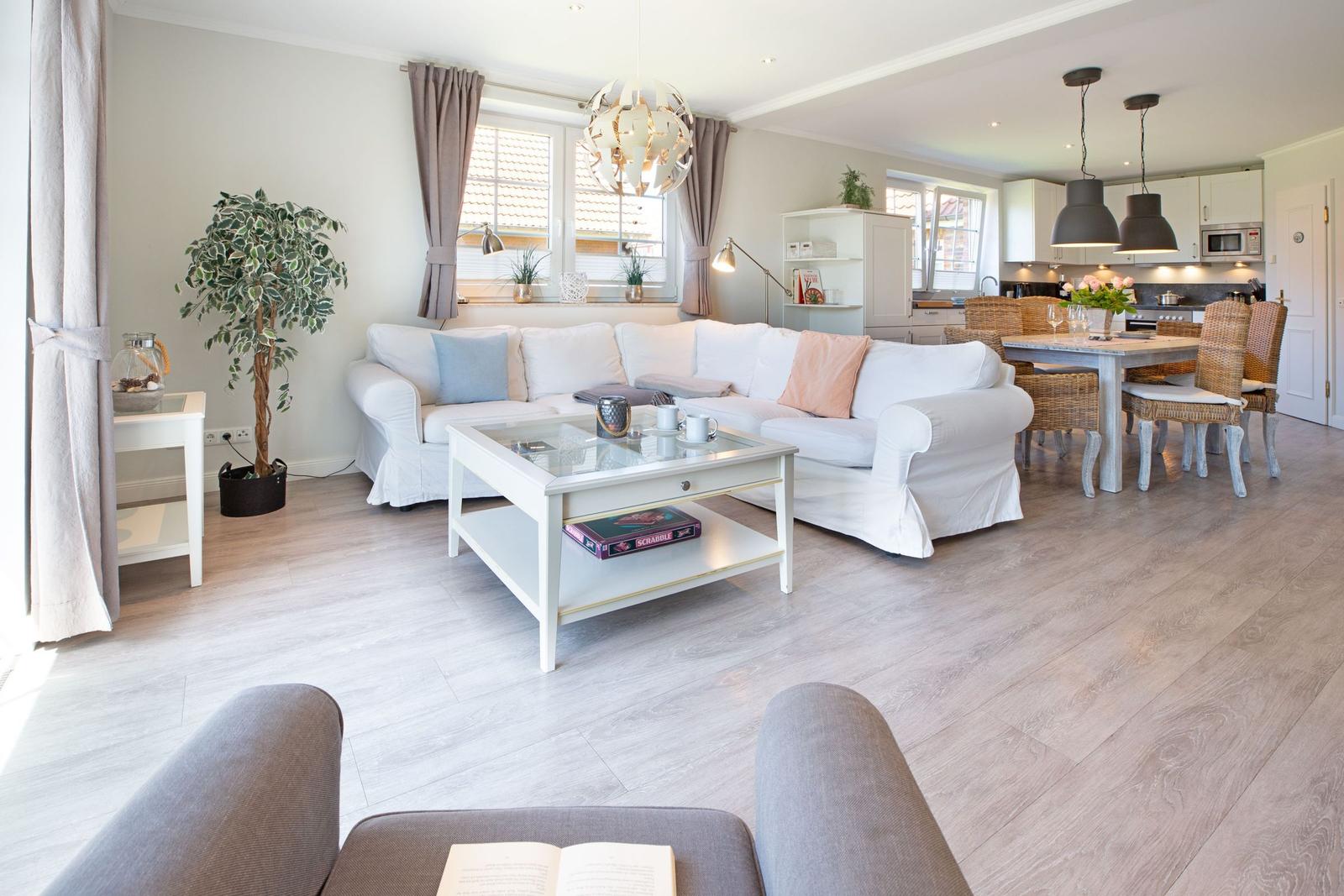 Wohn- und Essbereich mit weißem Sofa, Glas-Tisch und Küchenbereich im Hintergrund.
