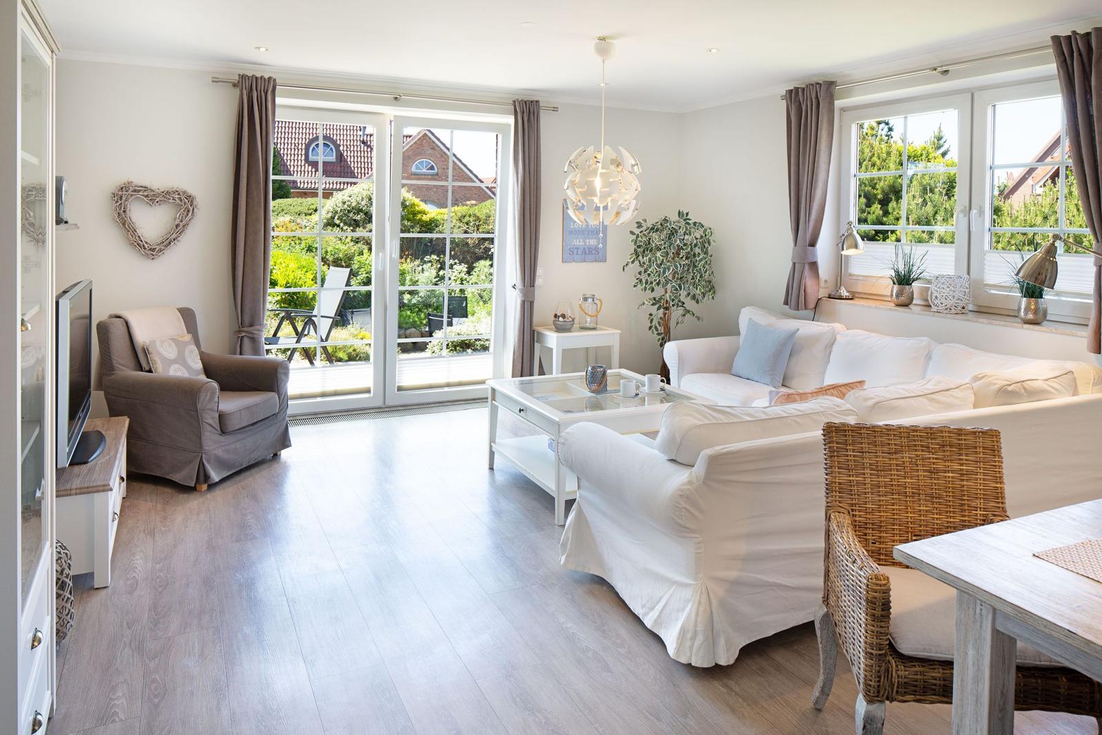 Wohnzimmer mit Sofa, Sessel und Blick auf Garten. Holzboden und Fensterfront.