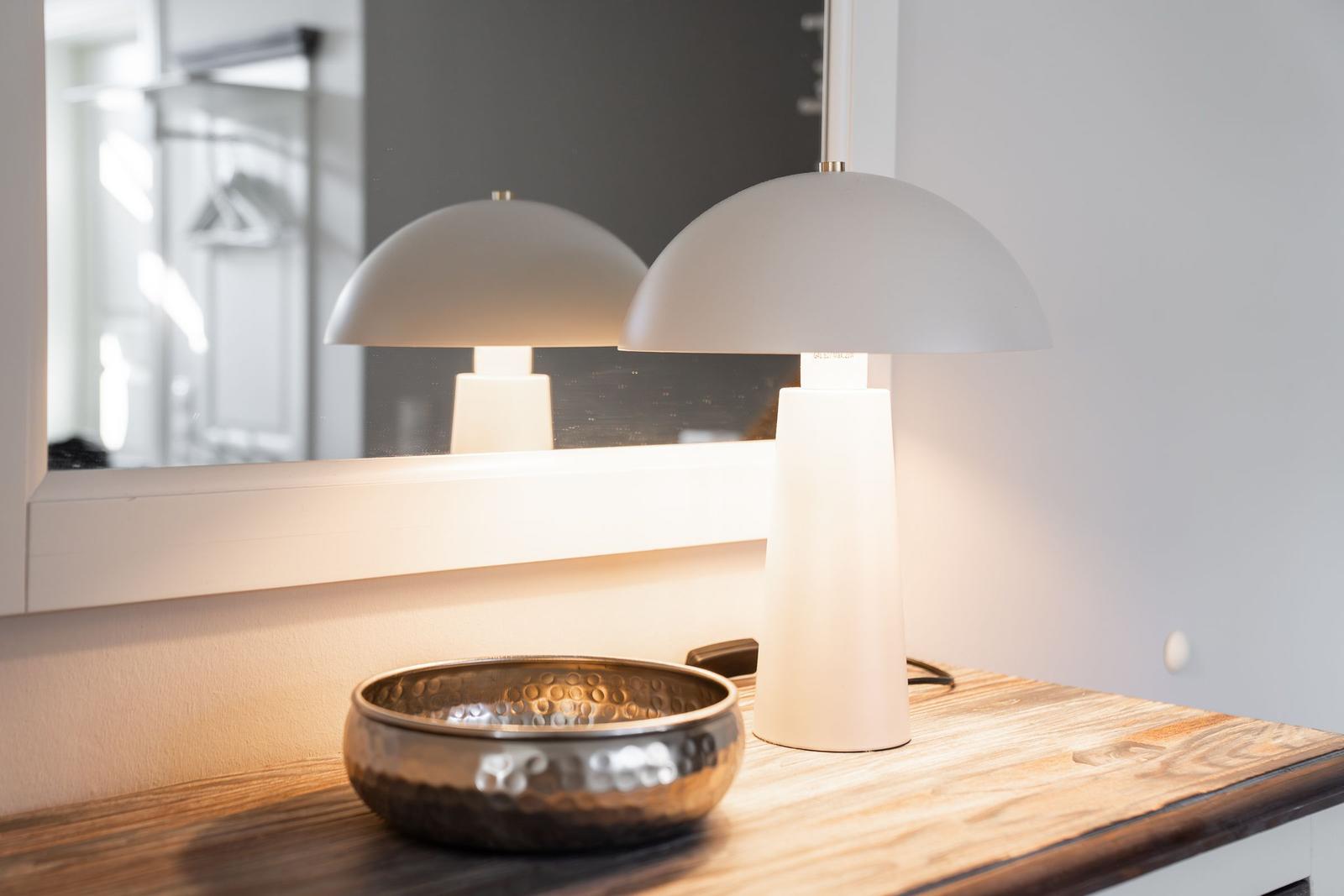Eine Lampe und eine Schale stehen auf einem Holztisch vor einem Spiegel.
