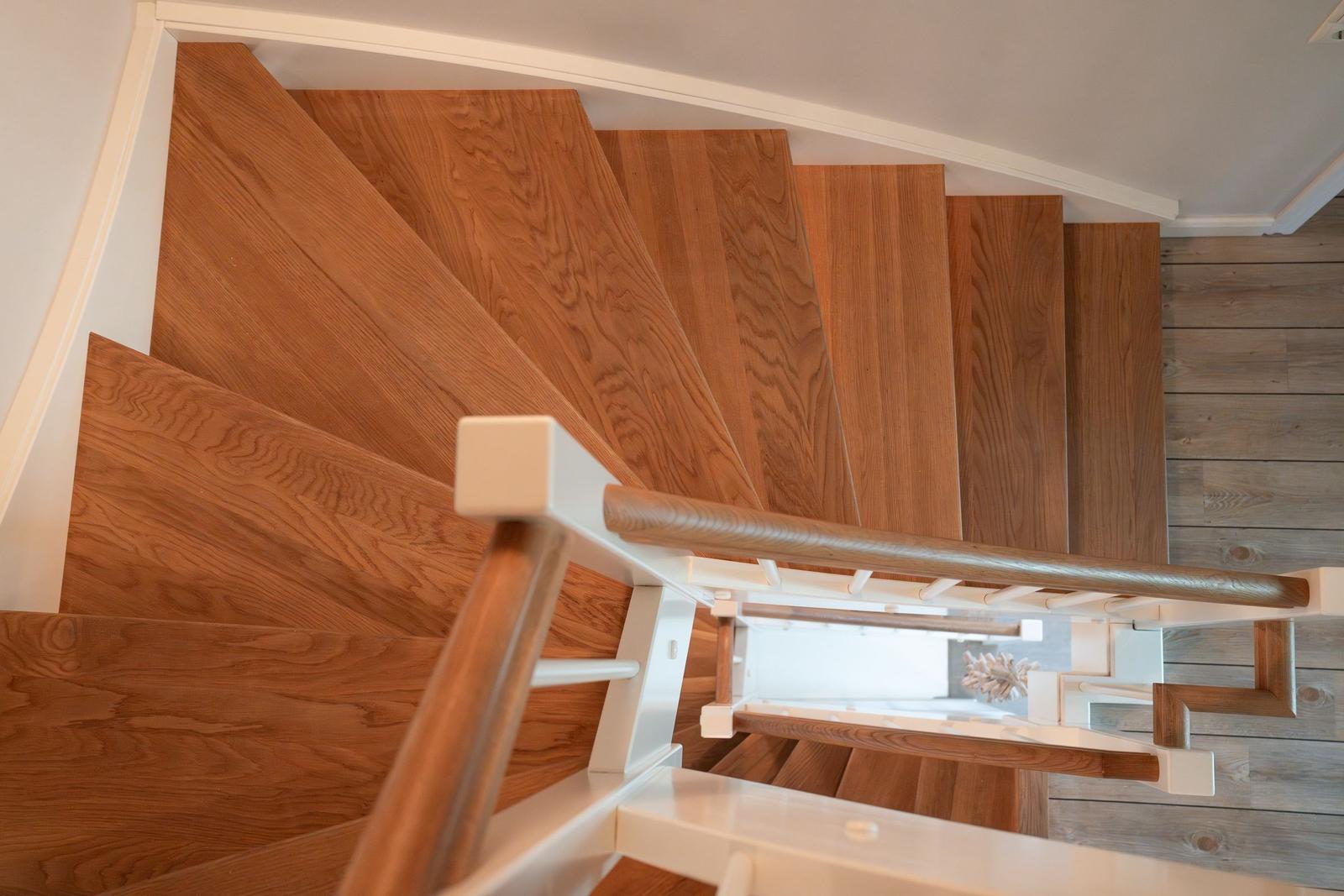 Holzgetäfelte Treppe mit weißem Geländer und Holzstufen. Blick in den unteren Bereich.