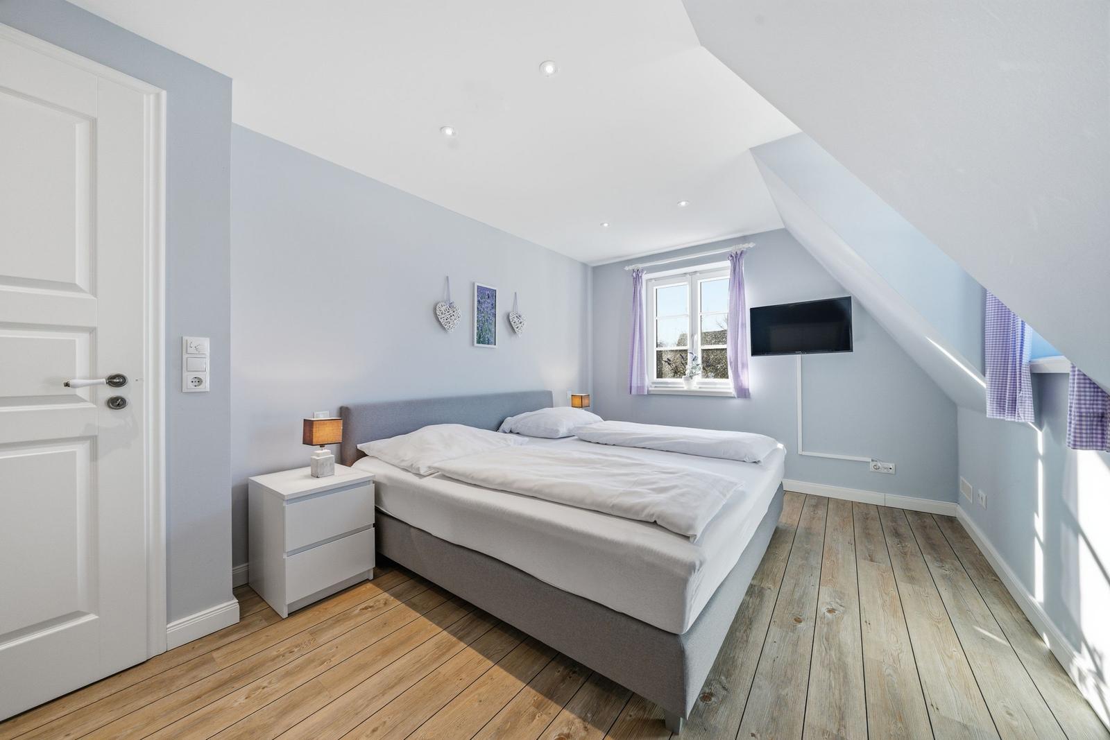 Schlafzimmer mit Dachschräge, Bett, Nachttisch und TV.