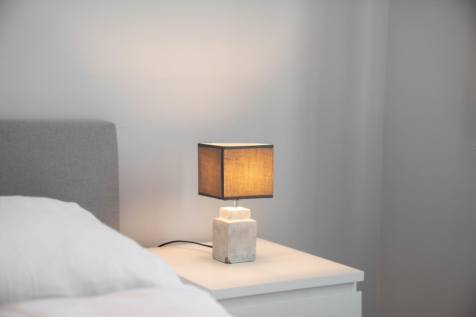 Schlafzimmer mit Nachttisch und Lampe. Bett mit Kopfteil und Bettwäsche.