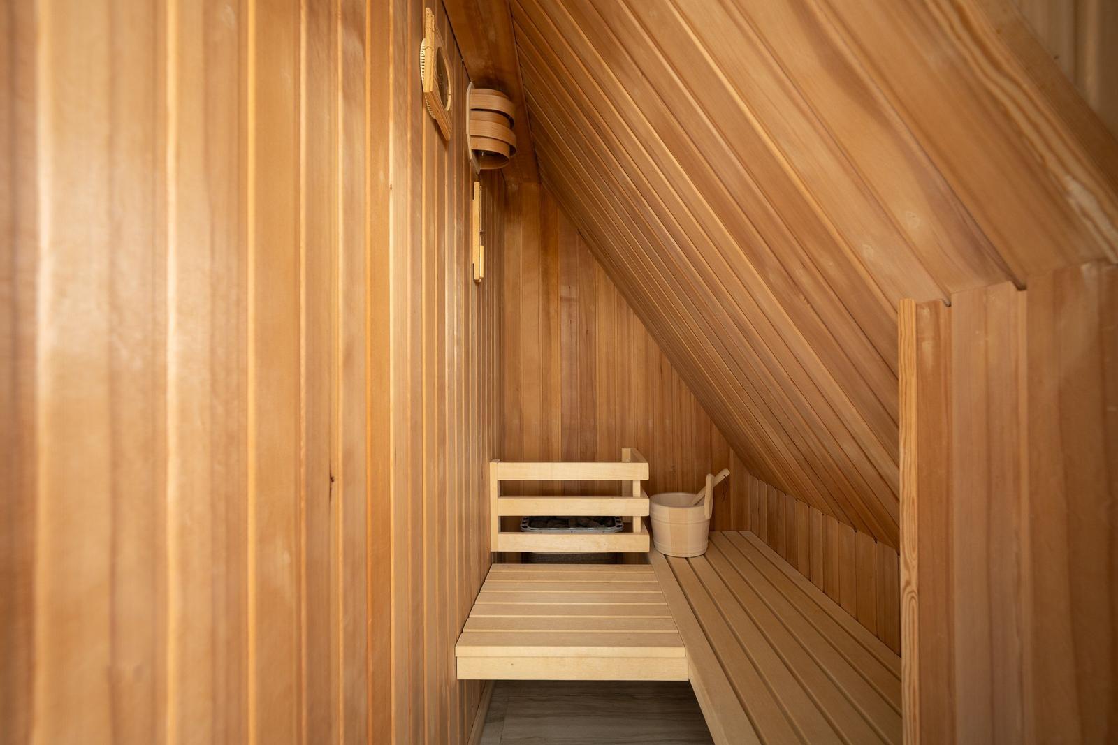 Holzsauna mit Sitzbänken und Eimer. Dachschräge und vertikale Holzwände.