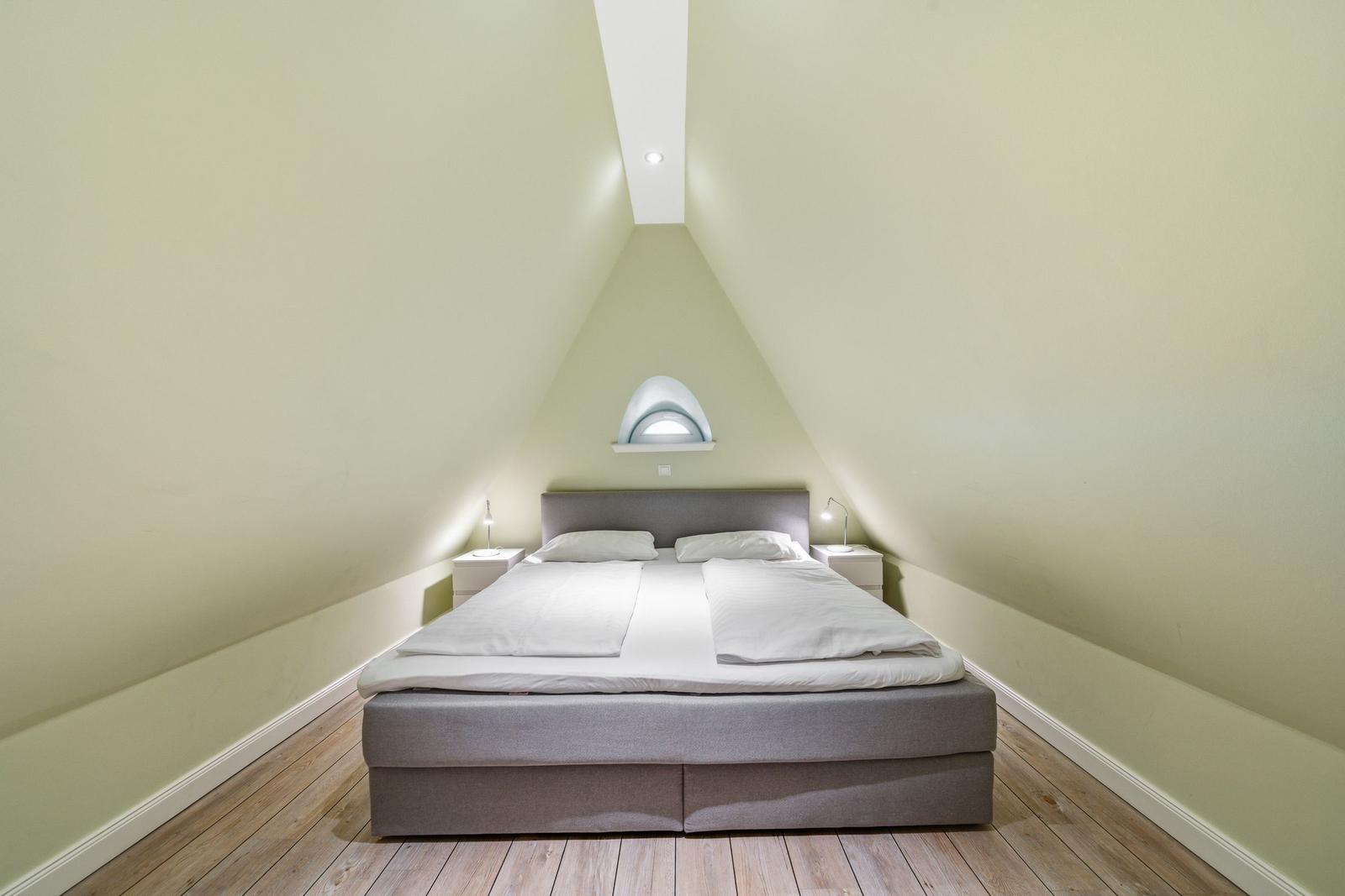Schlafzimmer mit Dachschrägen, Bett, Nachttischen und Fenster.
