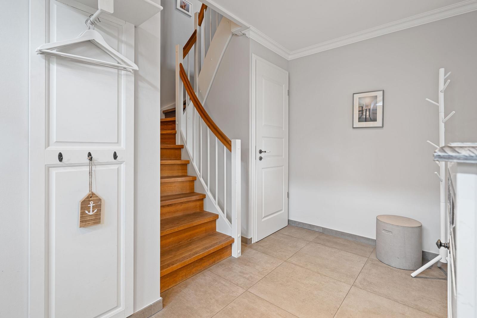 Eingangsbereich mit Holztreppe, weißen Türen und Garderobe mit Haken.