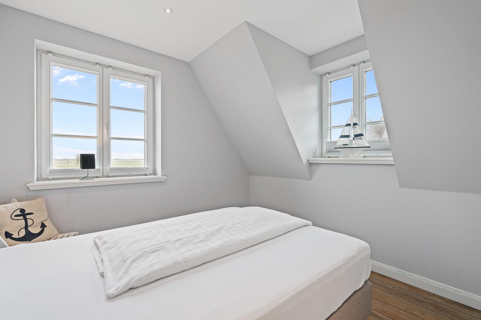 Schlafzimmer mit Dachfenster, weißem Bett und Blick auf Feld.