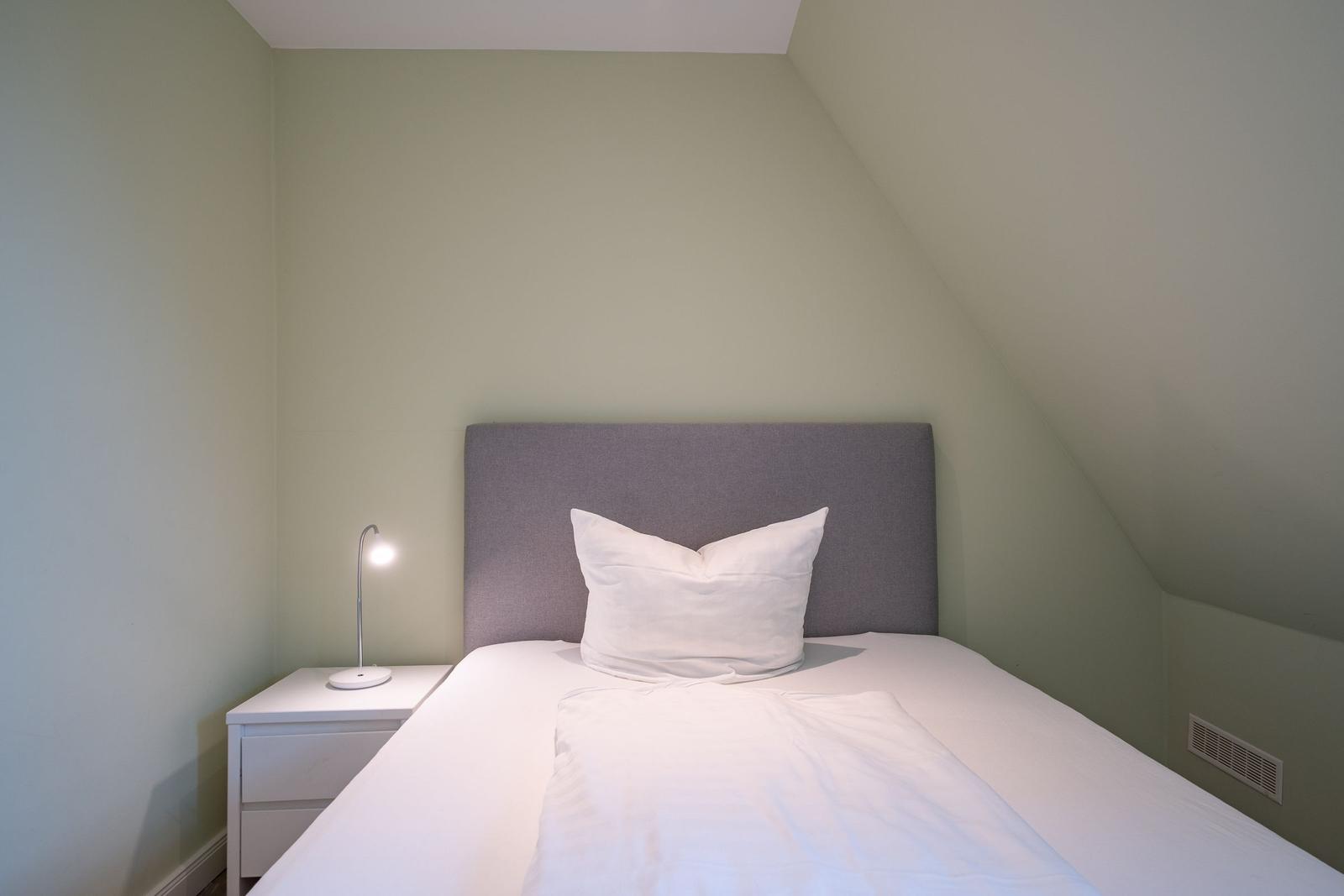Schlafzimmer mit Dachschrägen, weißem Bett und Nachttisch mit Lampe.