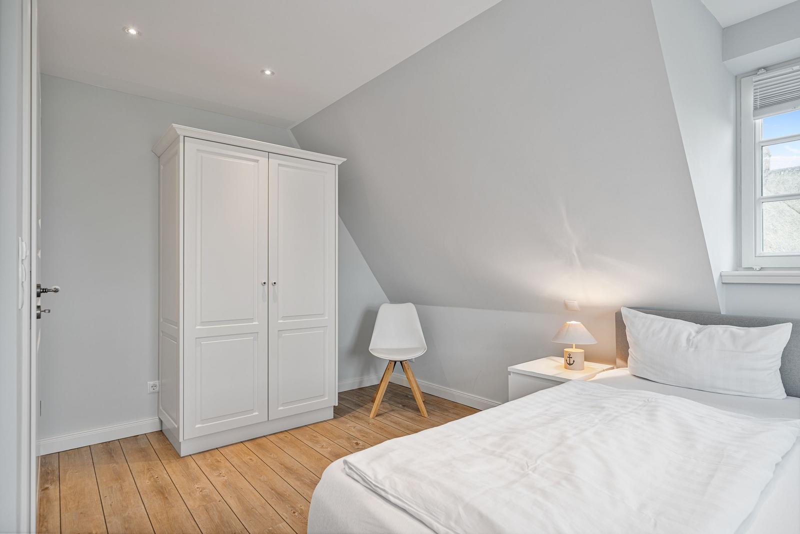 Schlafzimmer mit Dachschräge, weißem Schrank, Bett und Nachttisch.