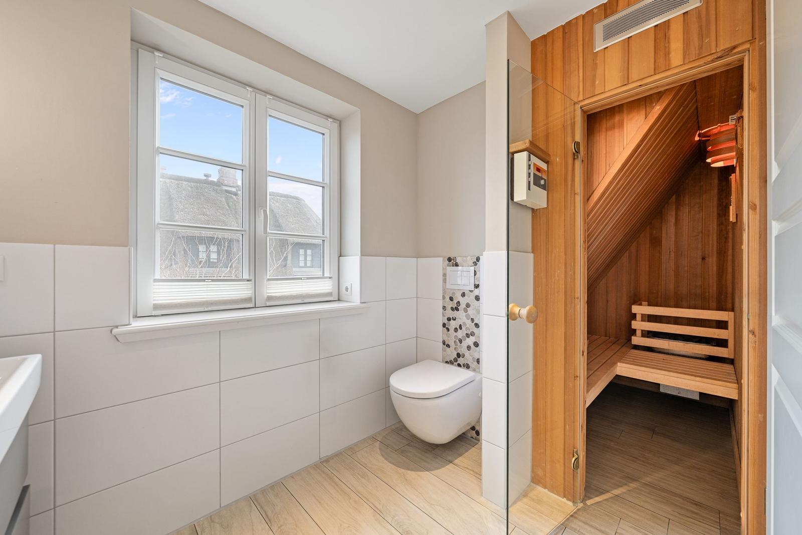 Badezimmer mit Toilette, Fenster und integrierter Holzsauna.