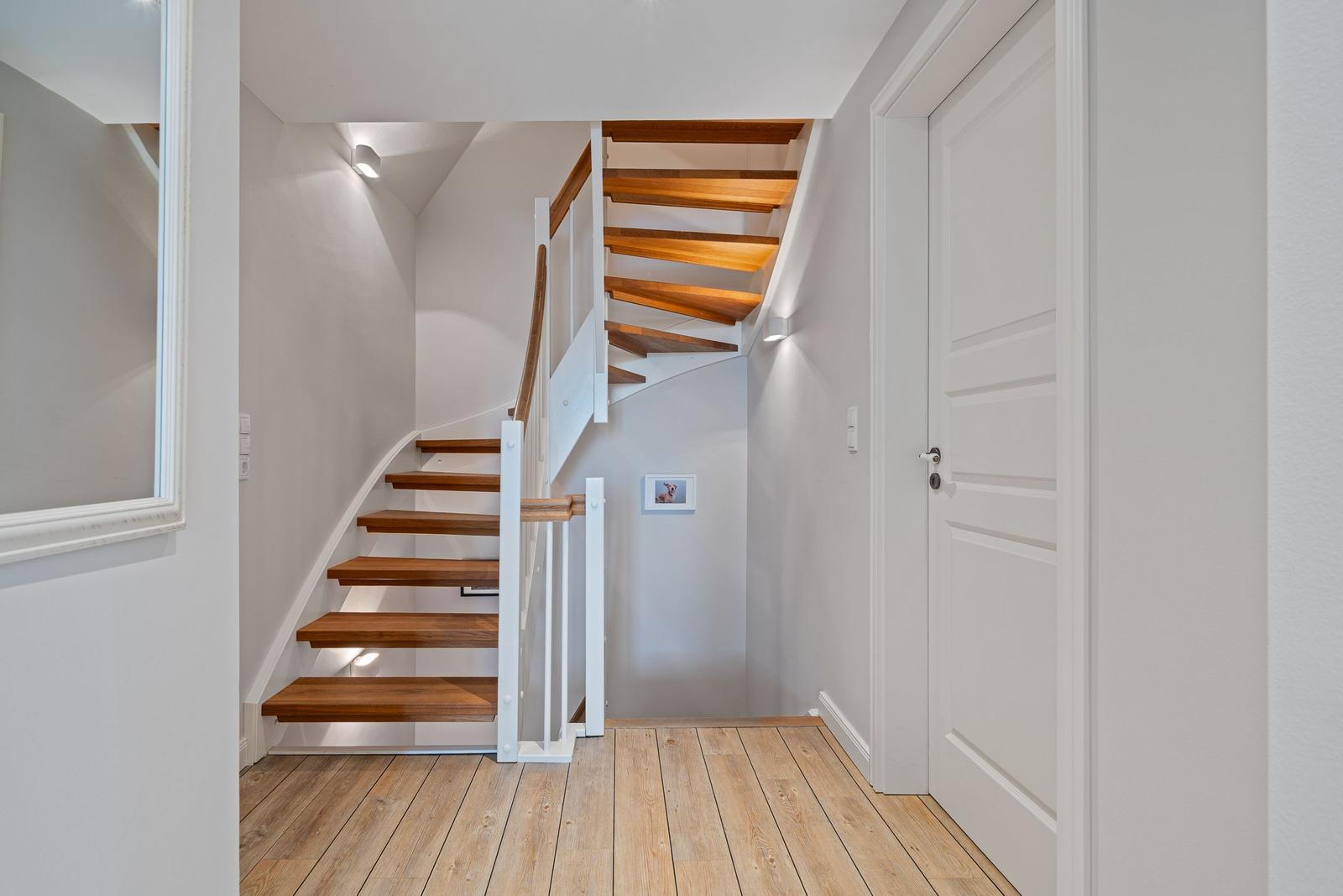 Holzgetriebene Treppe mit weißem Geländer führt nach oben. Holzfußboden und weiße Wände.