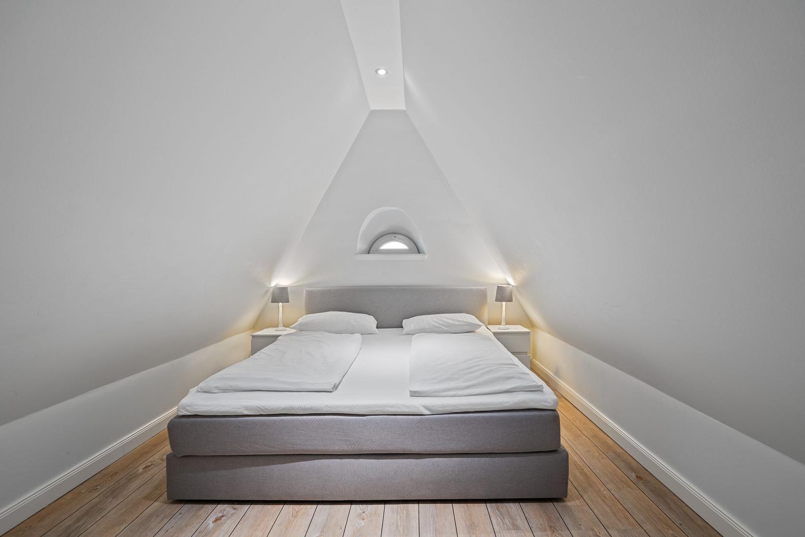 Schlafzimmer mit Doppelbett, Holzboden und schrägen Wänden. Zwei Nachttische mit Lampen.
