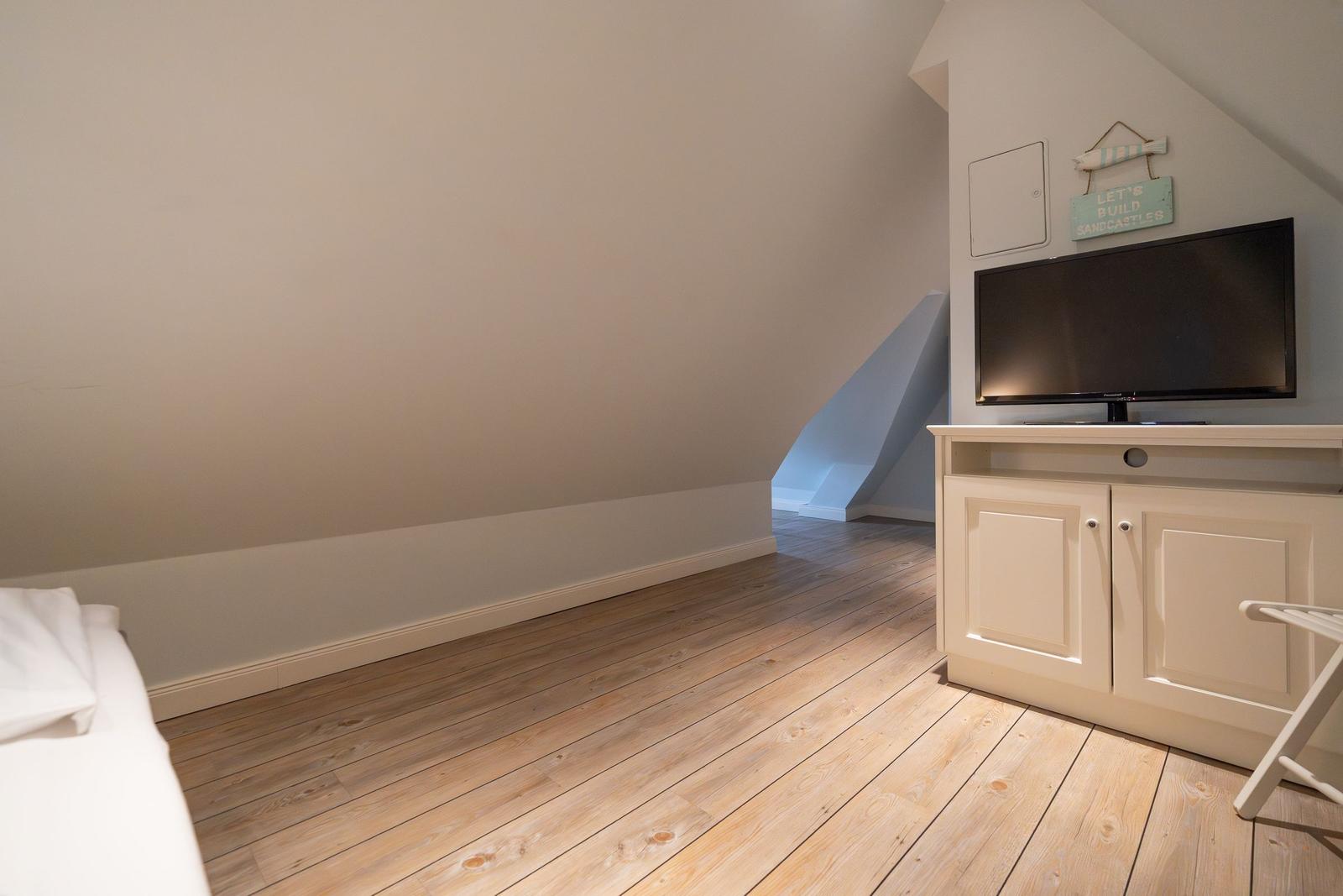 Schlafzimmer mit Holzboden, Fernseher und Schrank unter schrägen Wänden.