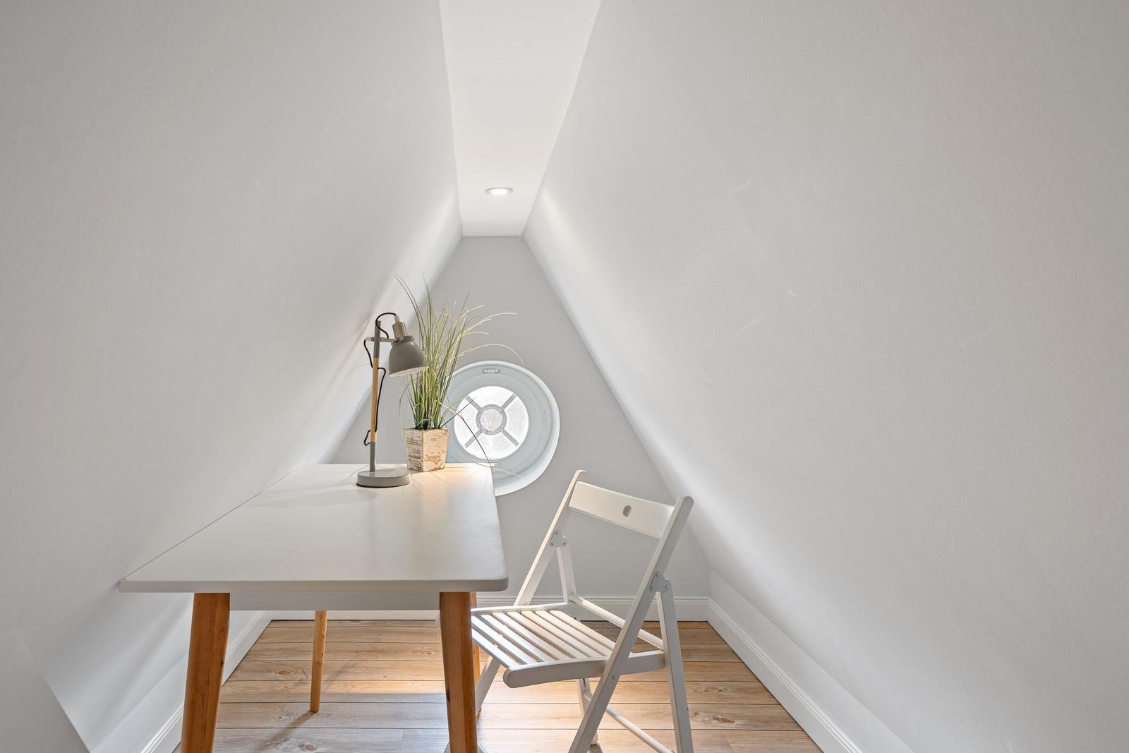 Arbeitszimmer mit Tisch, Stuhl und Rundfenster unter Dachschrägen.