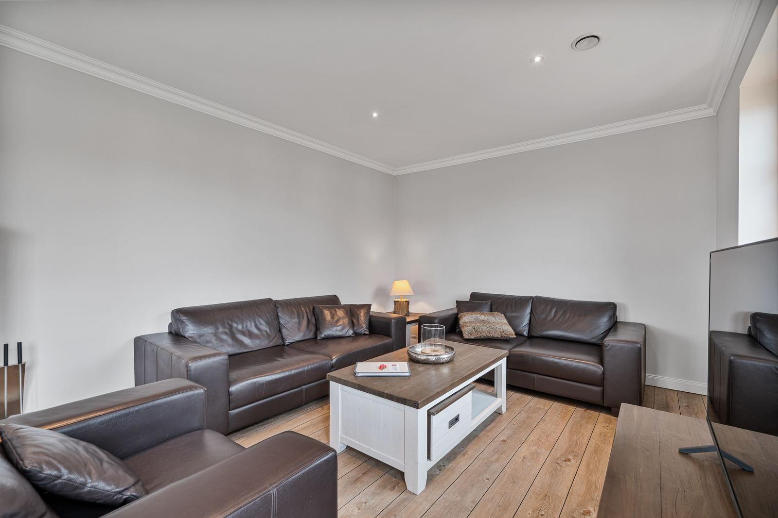 Wohnzimmer mit braunen Ledermöbeln, Holzboden und weißem Couchtisch.