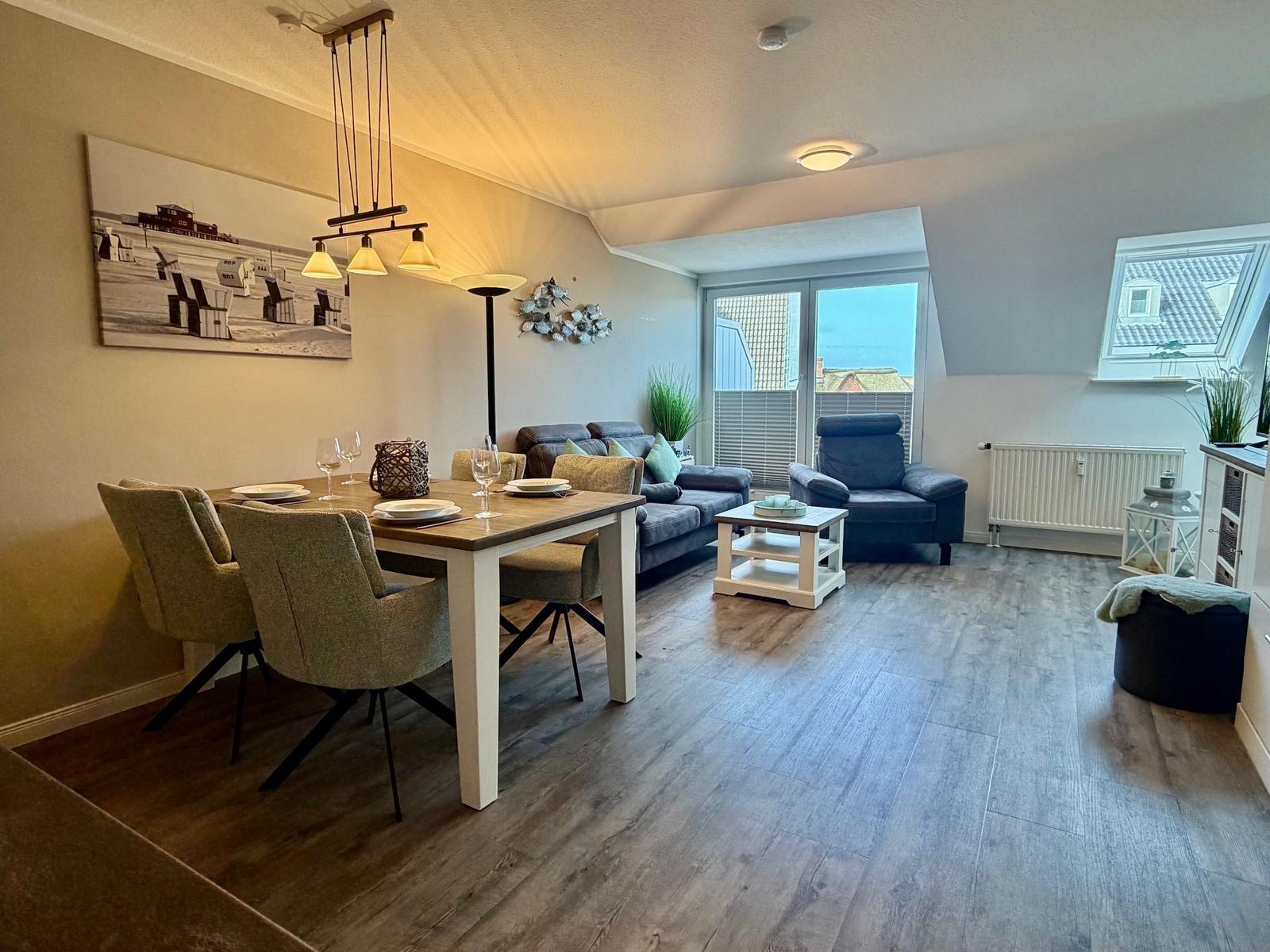 Essbereich mit Tisch und Stühlen, Wohnbereich mit Sofa und Sessel, Holzboden und große Fenster.