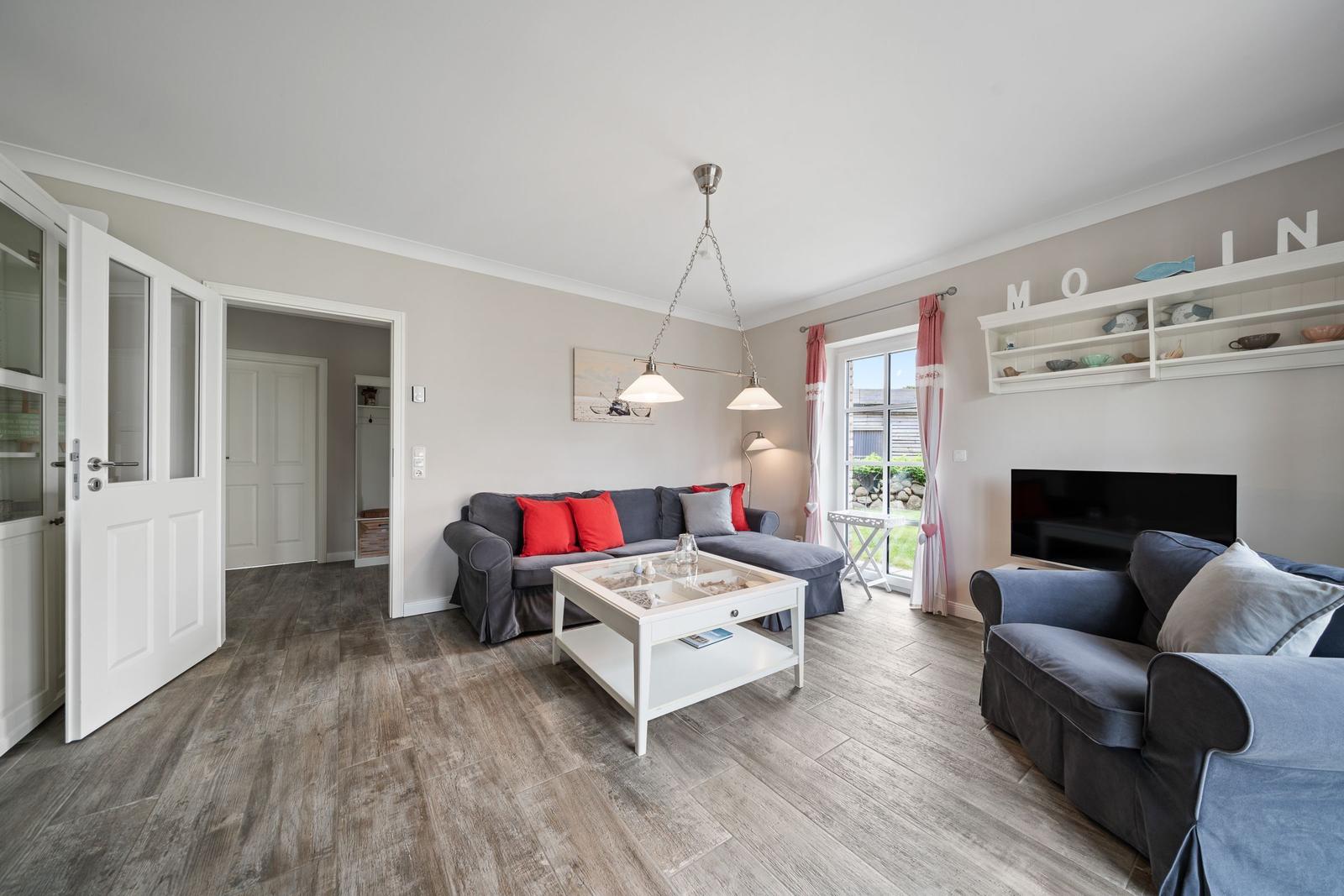 Wohnzimmer mit grauem Sofa, weißem Couchtisch und Fernseher an der Wand.