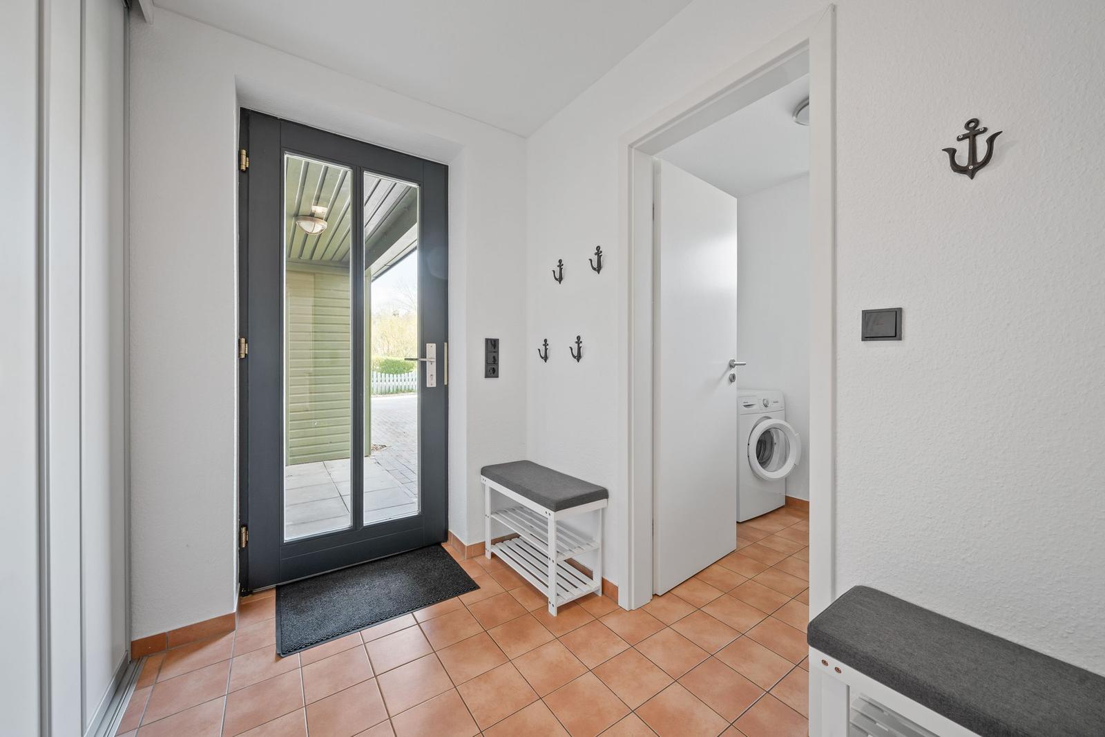 Eingangsbereich mit Glastür, Schuhschrank und Waschmaschine im Hintergrund.