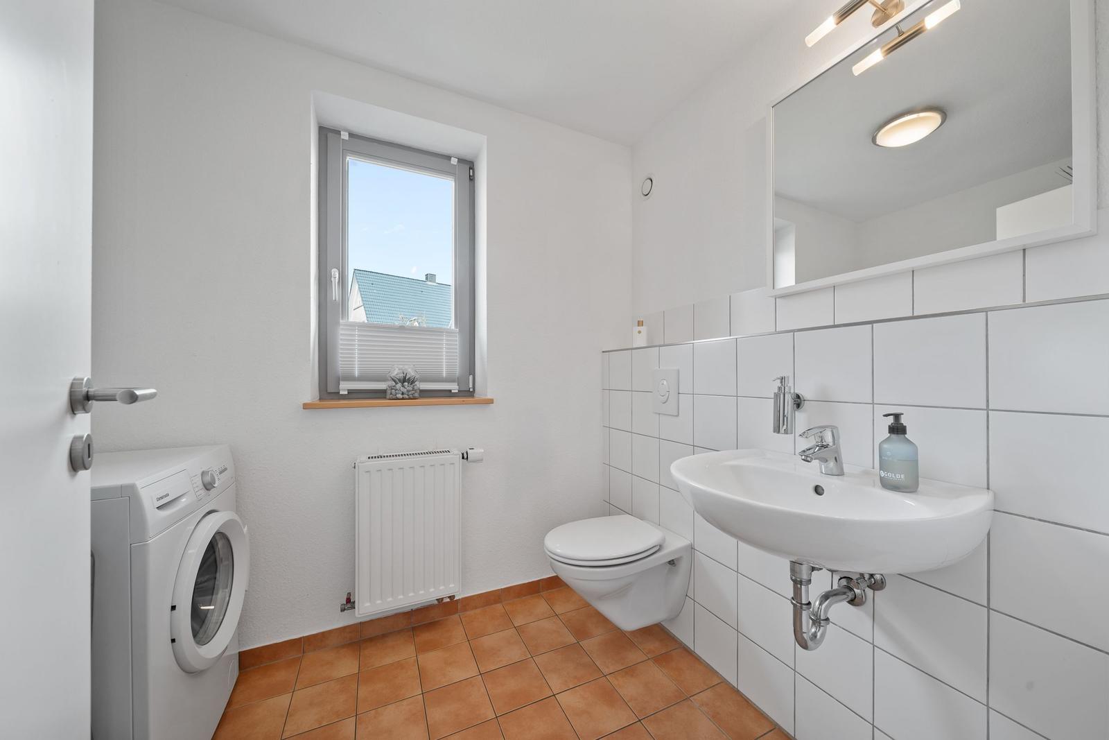 Badezimmer mit Waschmaschine, Toilette und Fenster