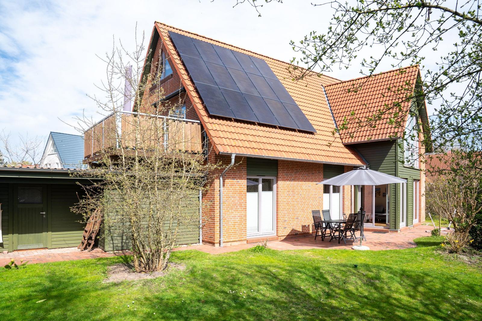 Haus mit Solaranlage, Terrasse und Garten. Holzterrasse und grüner Rasen.