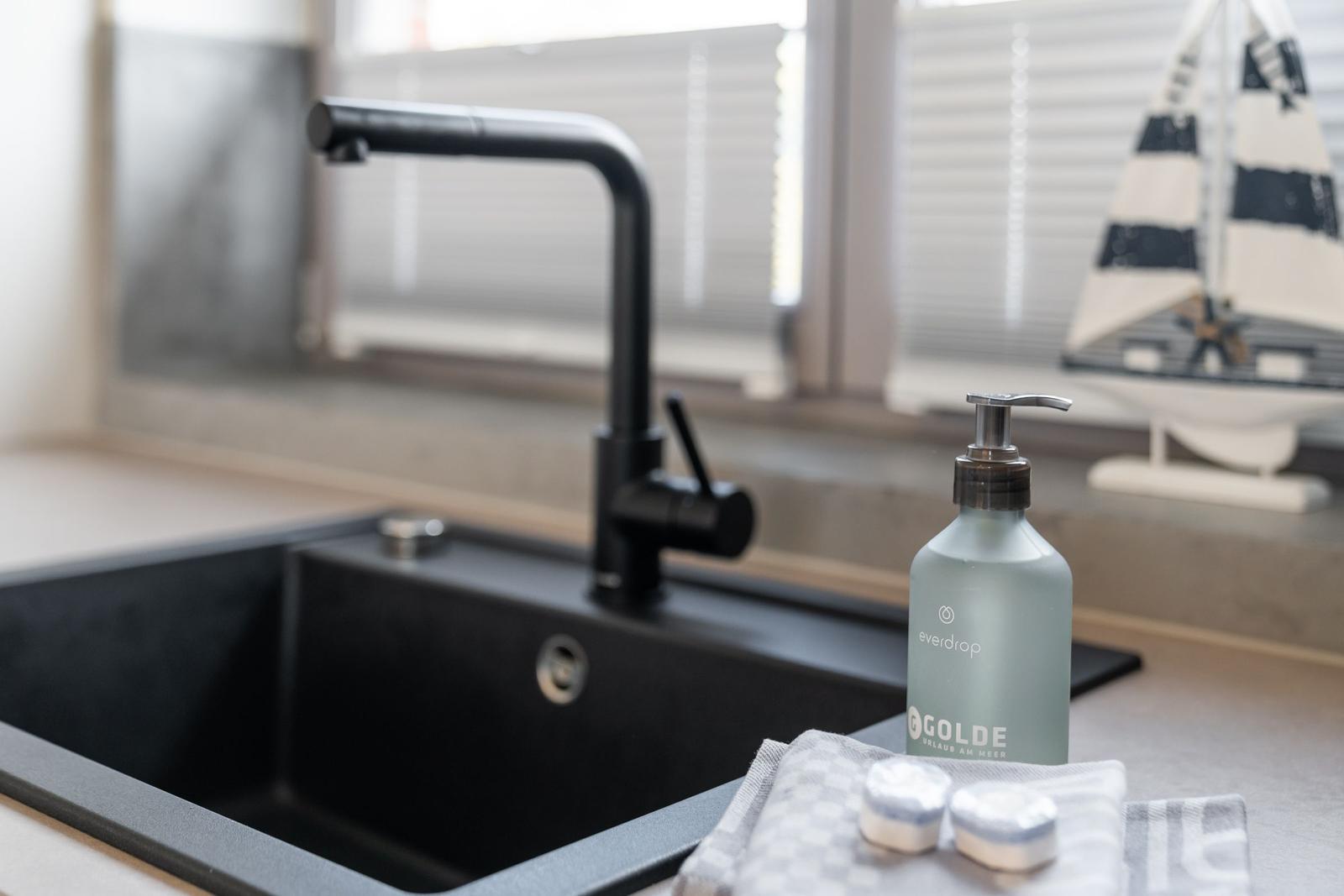 Schwarzes Waschbecken mit modernem Wasserhahn und Seifenflasche auf Arbeitsplatte.