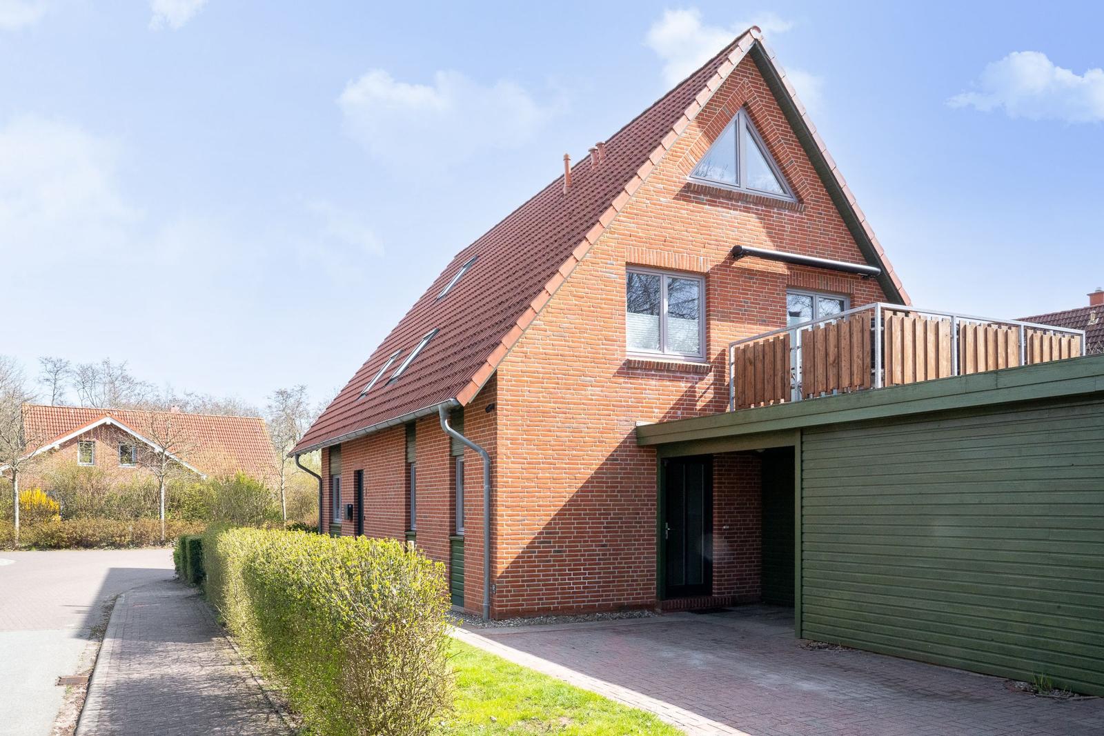 Rotes Ziegeldach, Holzveranda und grüner Anbau an einem zweistöckigen Haus.