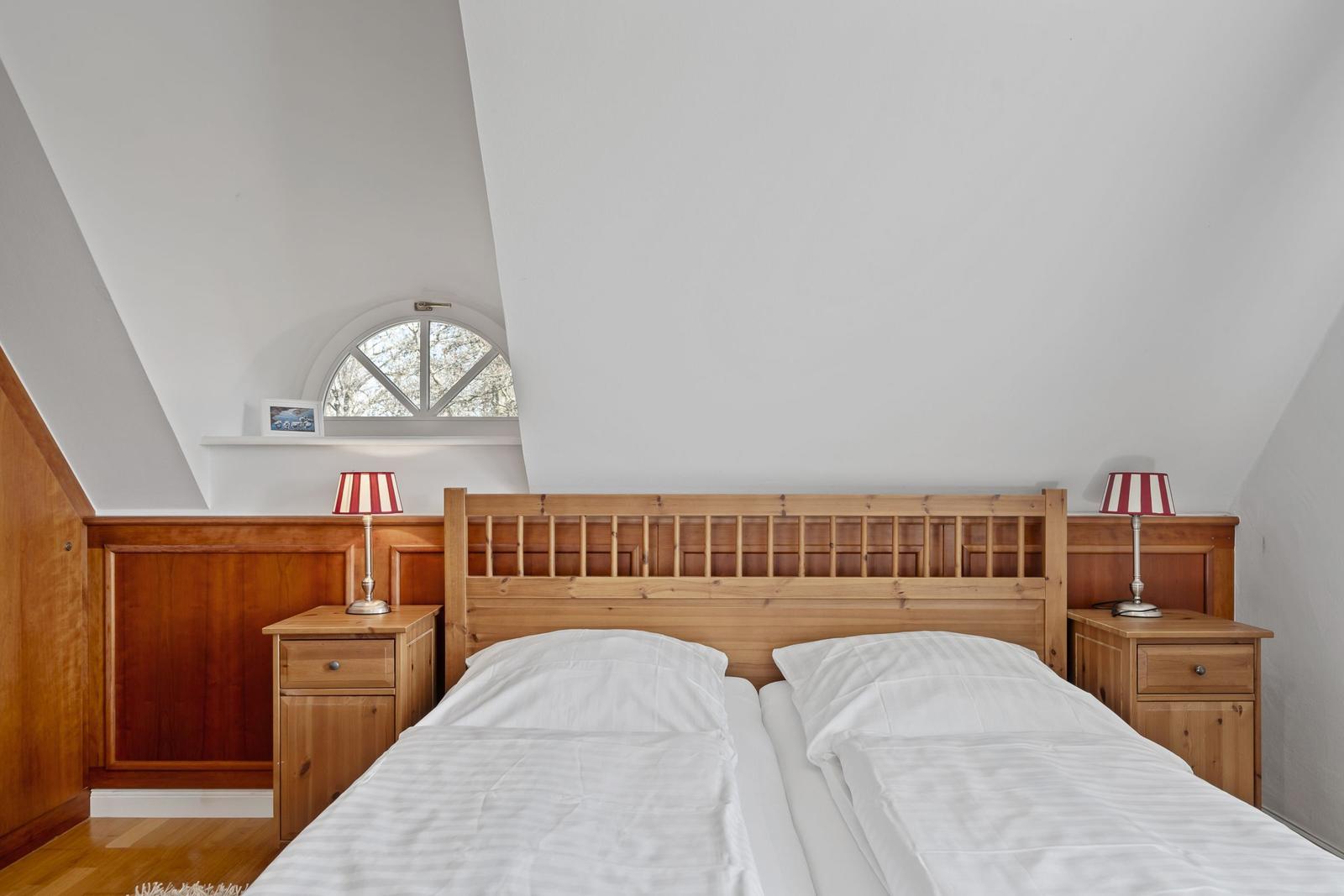 Doppelbett mit Holzgestell, zwei Nachttische und rote Lampenschirme unter schrägen Dachdecken.