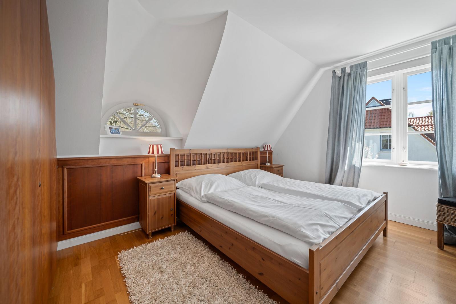 Schlafzimmer mit Holzbett, Nachttischen und Fenster. Holzfußboden und Schrank sind sichtbar.
