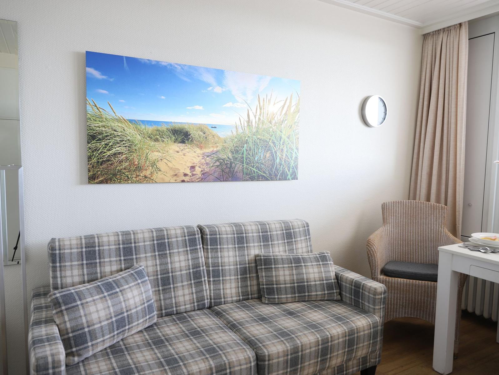 Ein Wohnzimmer mit Sofa, Stuhl und Wandbild von Strand.