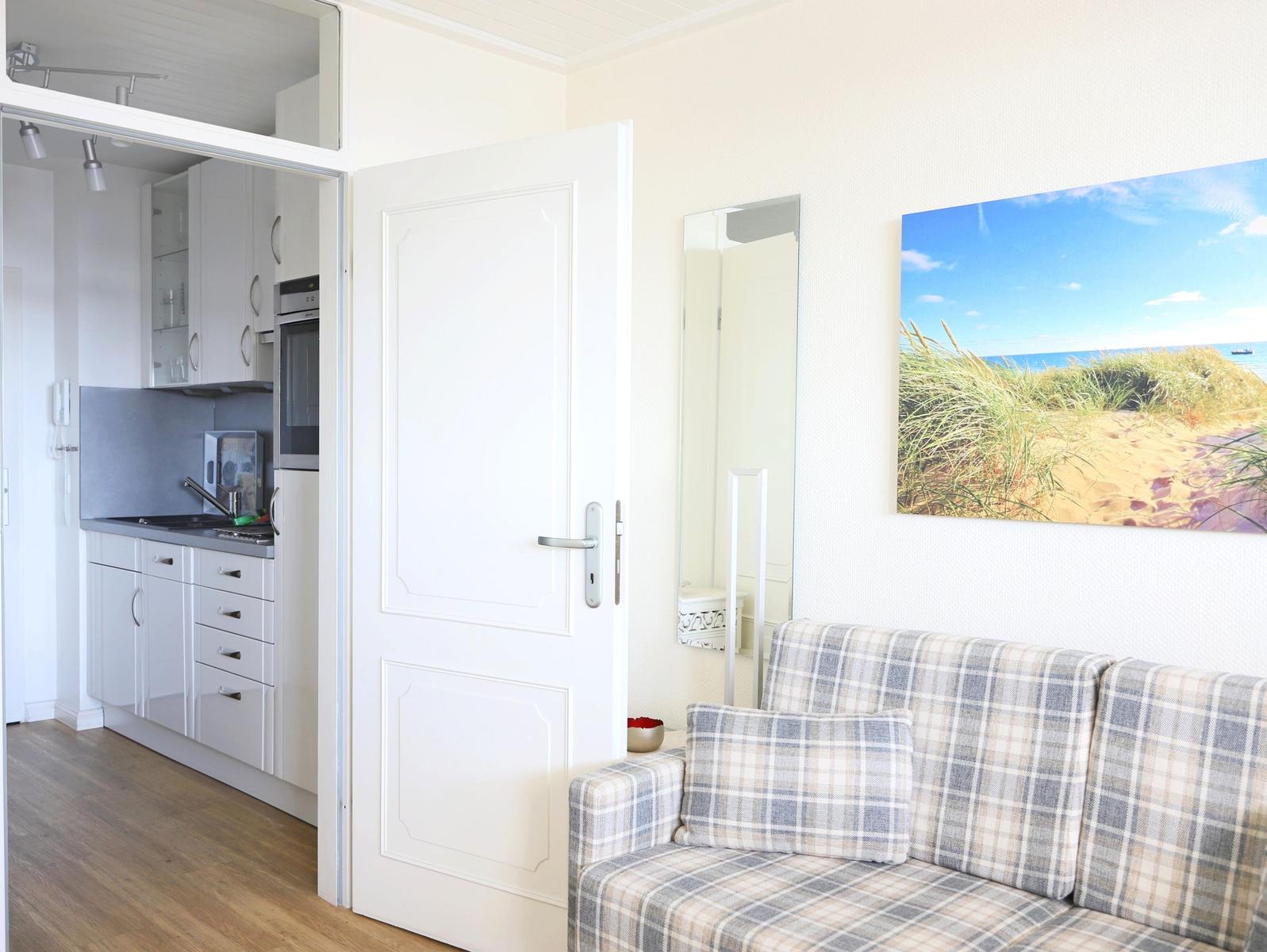Wohnzimmer mit Sofa und Küchenbereich im Hintergrund. Wandbild zeigt Strand.