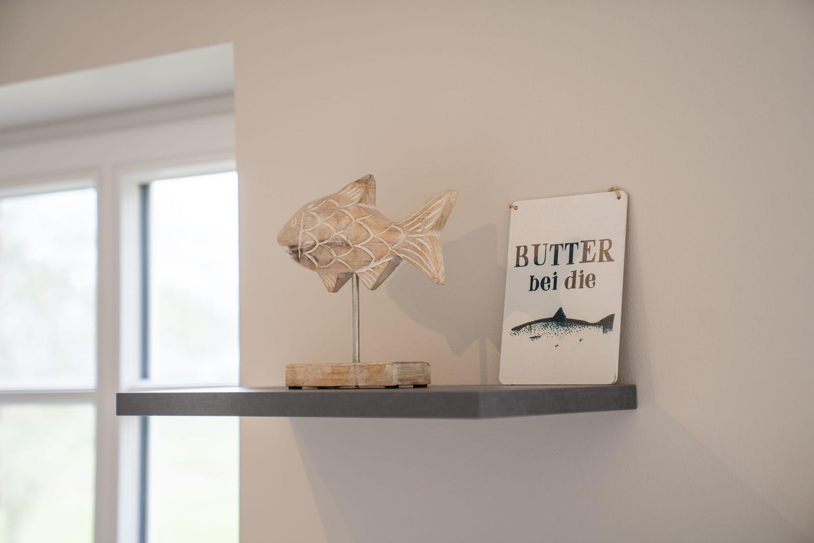 Holzfigur eines Fisches und Schild mit Schrift stehen auf einer Wandregal.