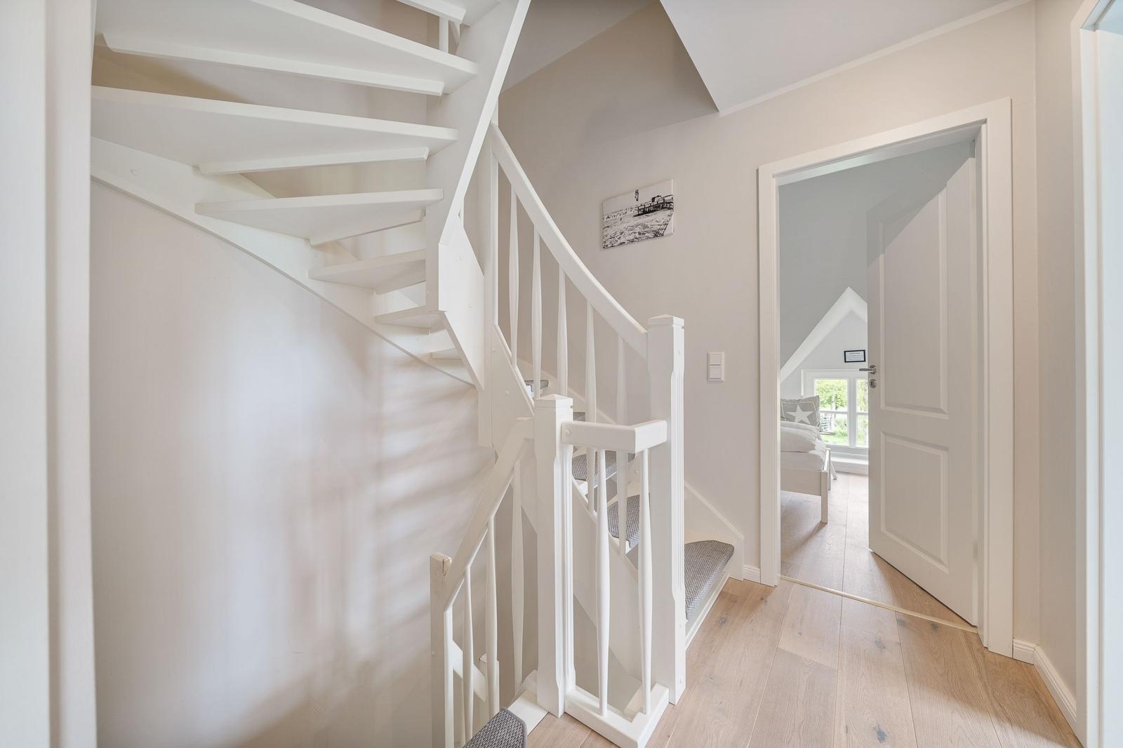 Helle Treppe mit weißer Balustrade führt zur Wohnung. Durch Tür ist Schlafzimmer mit Fenster sichtbar.