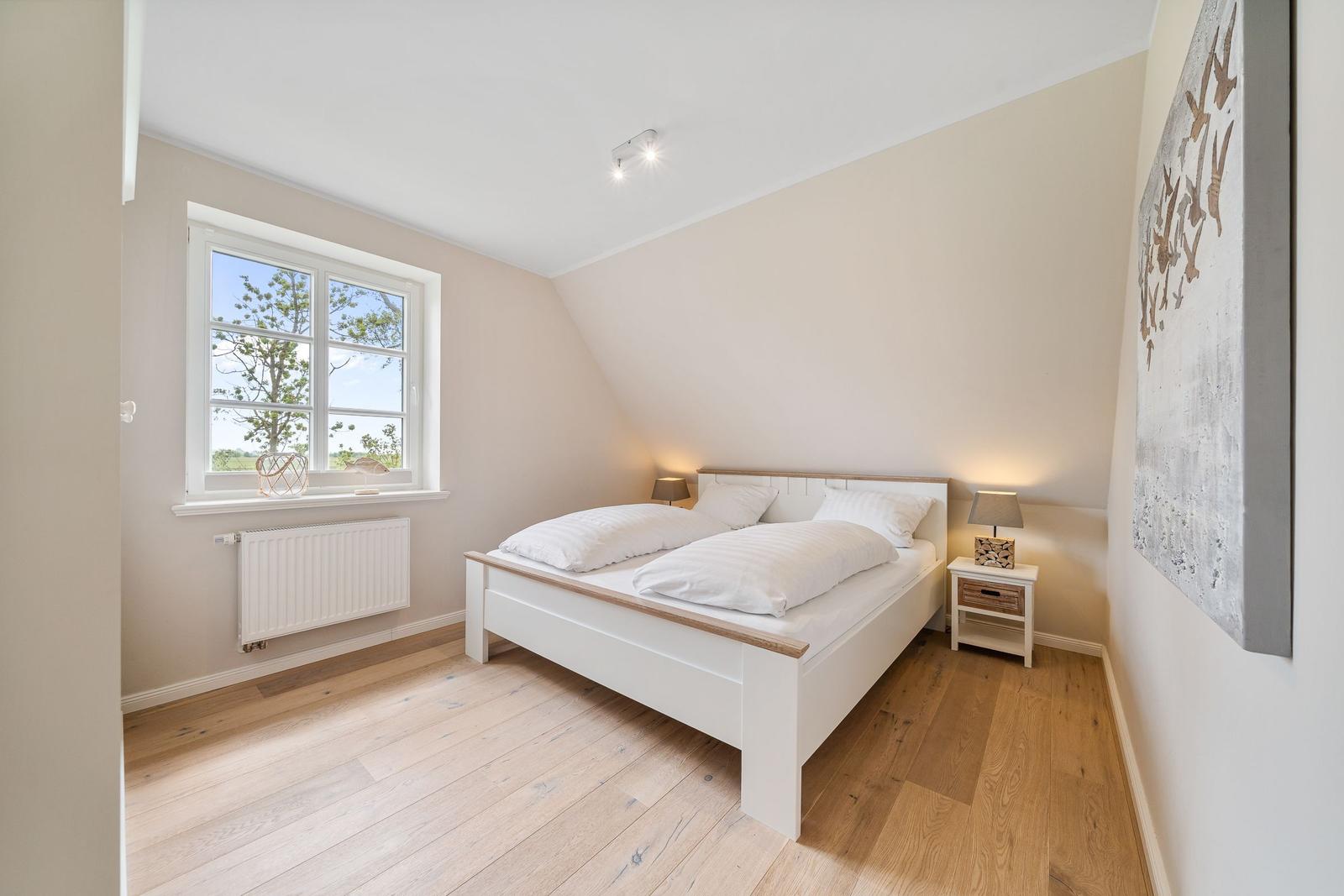 Schlafzimmer mit Doppelbett, Holzboden und Fenster mit Blick auf Grünfläche.