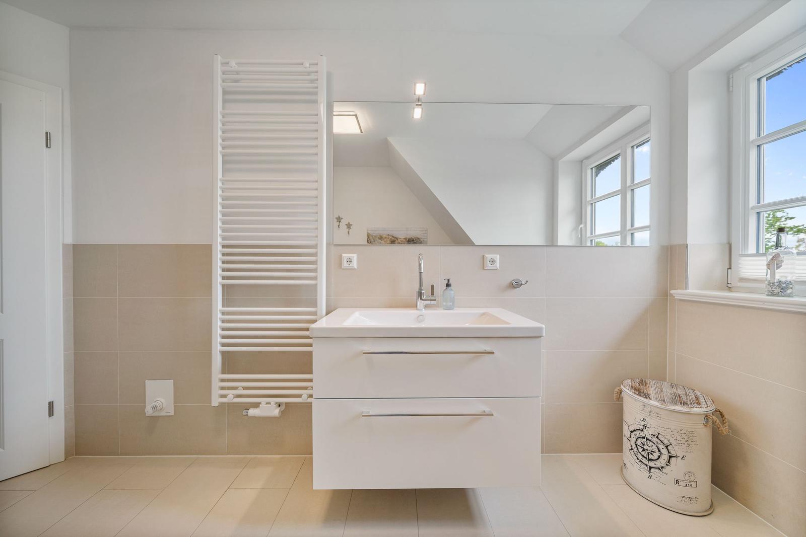 Badezimmer mit Waschbecken, Spiegel und Heizkörper an der Wand.