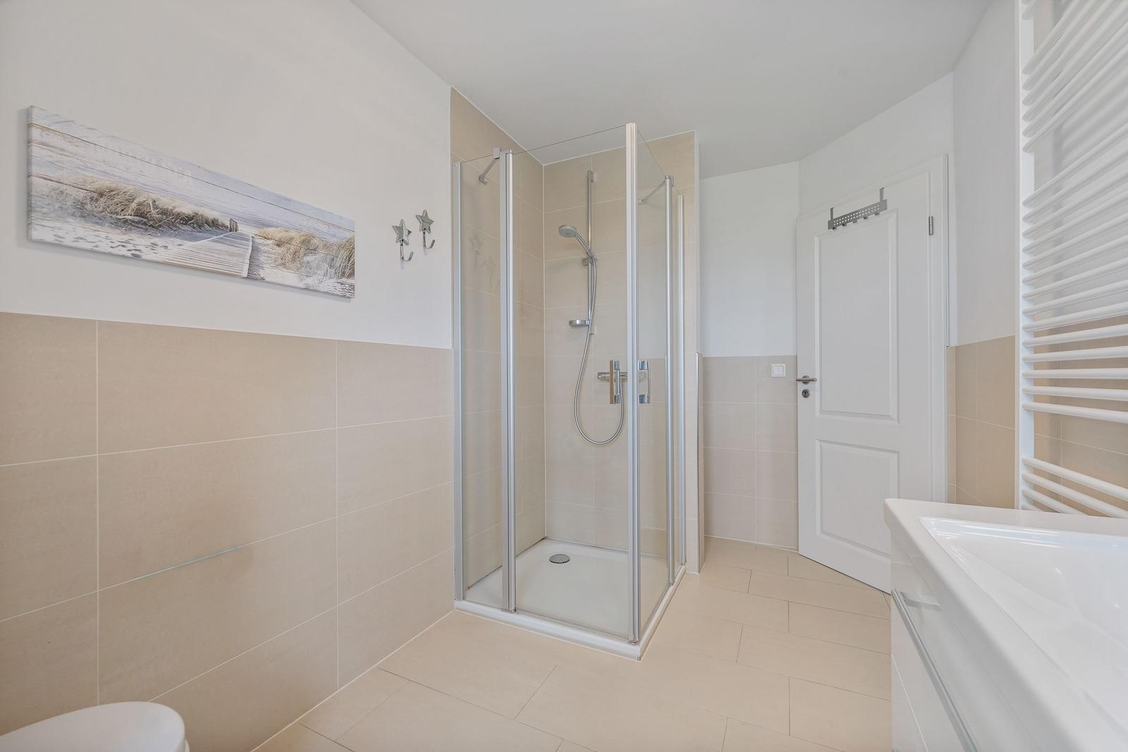 Badezimmer mit Dusche, Waschtisch und Heizung. Wandbild und Haken sichtbar.