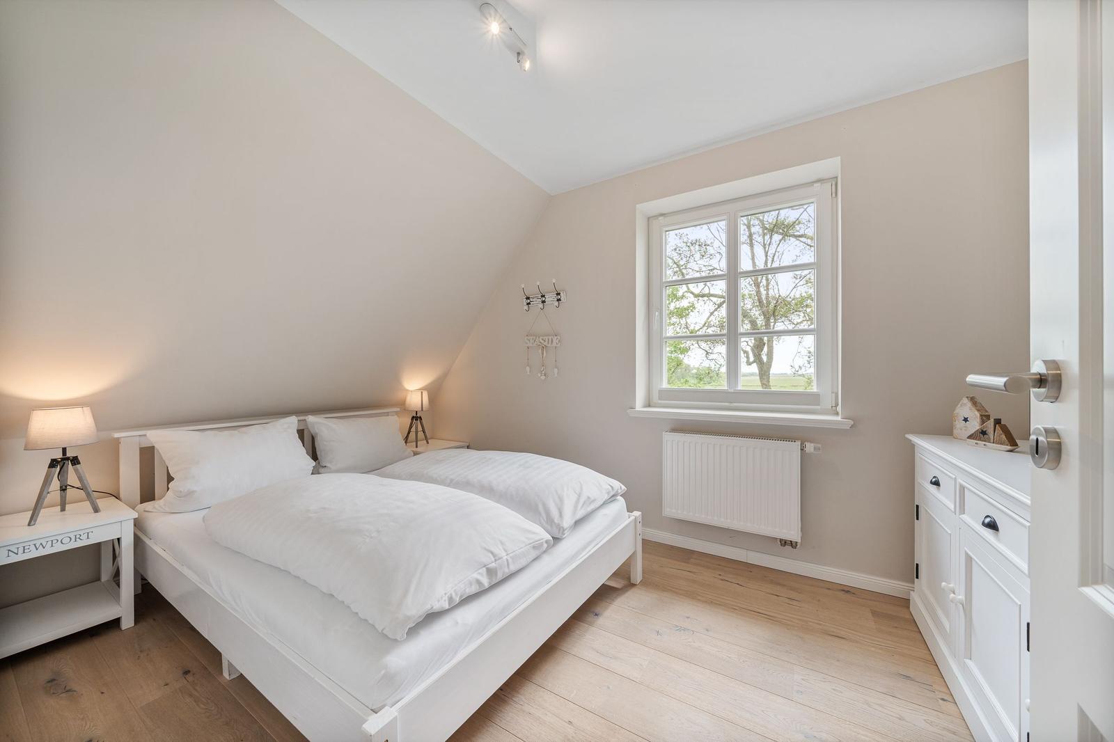 Schlafzimmer mit Dachschräge, weißem Bett, Holzboden und Fenster mit Blick auf Außenbereich.