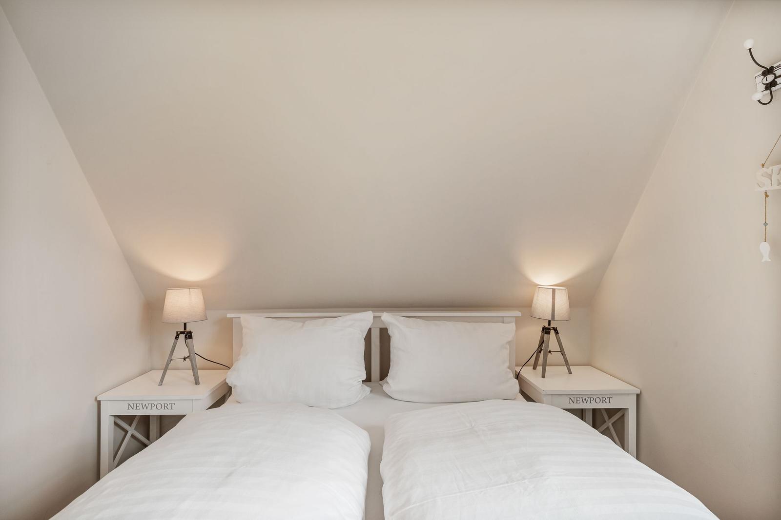 Schlafzimmer mit Doppelbett, zwei Nachttischen und Lampen unter schrägen Decken.