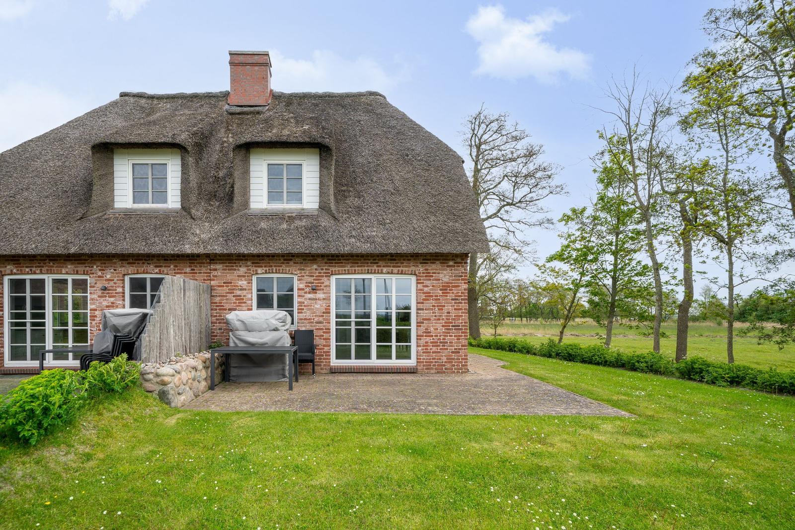 Haus mit Strohdach, Backsteinfassade und Terrasse mit Garten.