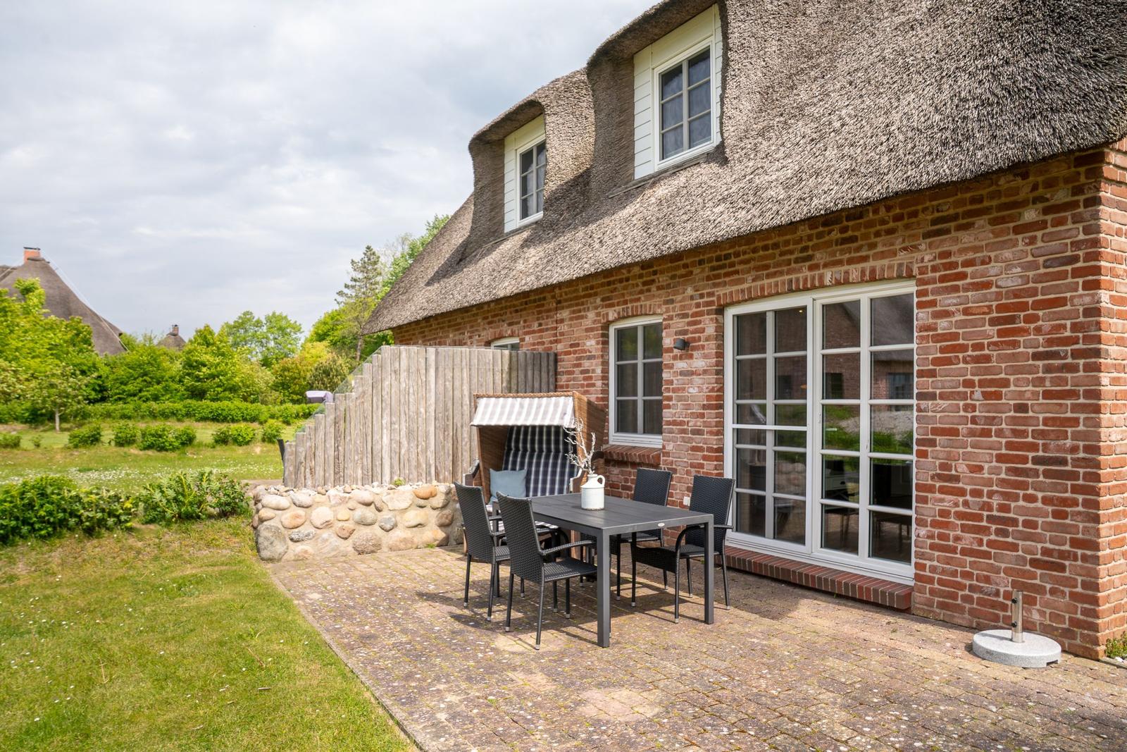 Haus mit Strohdach und Steinmauer, Terrasse mit Tisch und Stühlen.