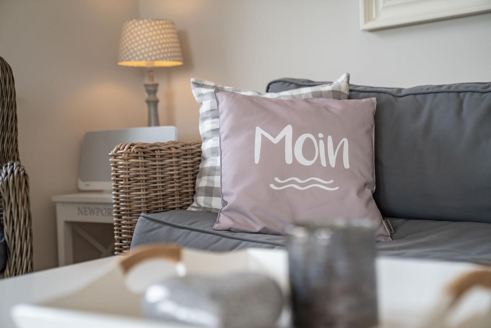 Graue Couch mit Kissen, das Moin schreibt, und einer Lampe im Hintergrund.