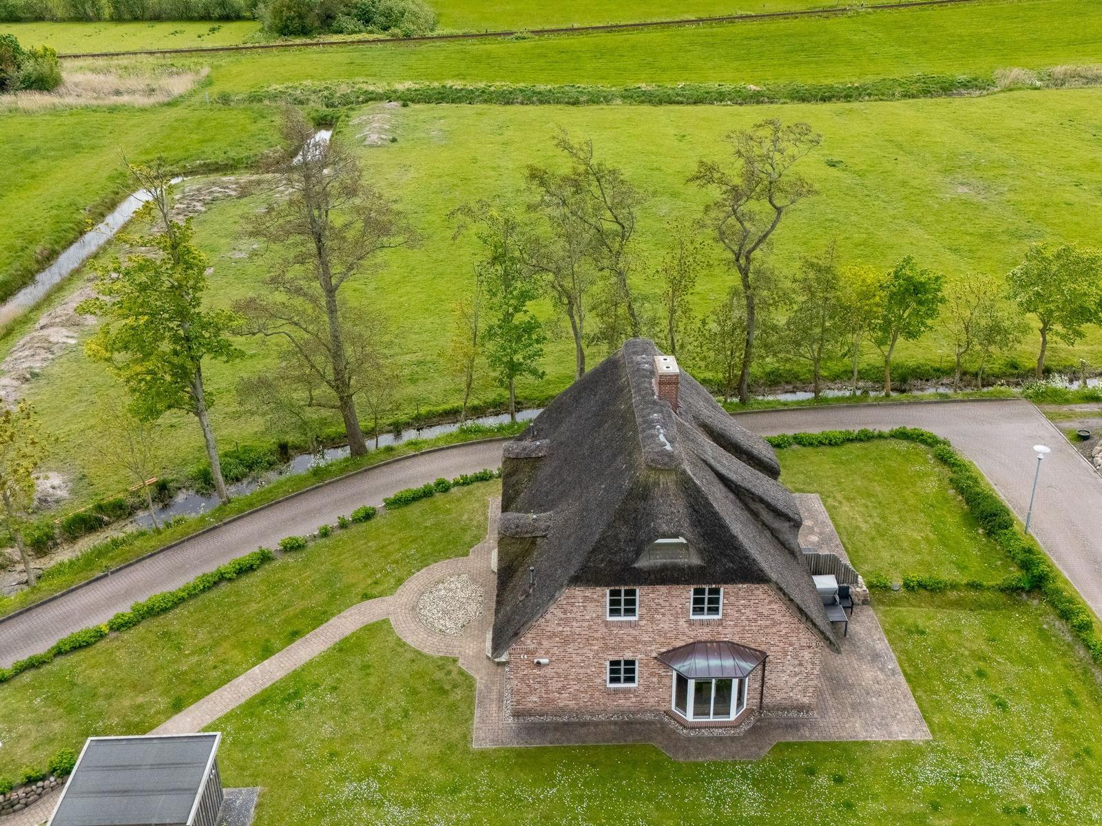 Haus mit Strohdach, umgeben von Grünflächen und einem Wassergraben.