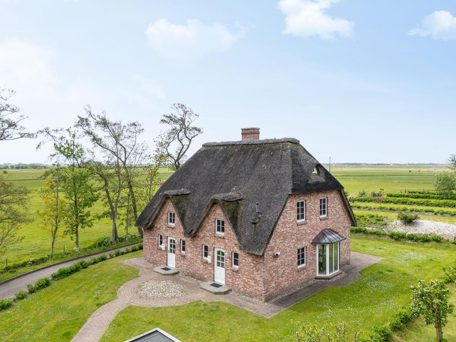 Haus mit Strohdach, Backsteinfassade und Garten. Umgeben von Wiesen und Bäumen.