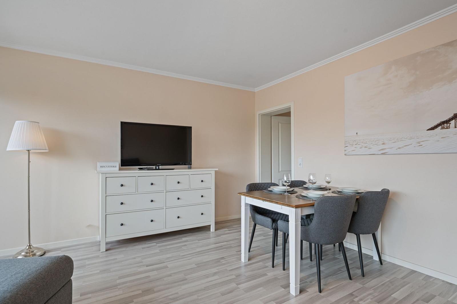 Esszimmer mit Tisch, Stühlen und Fernseher auf Schrank. Wandbild und Stehlampe.