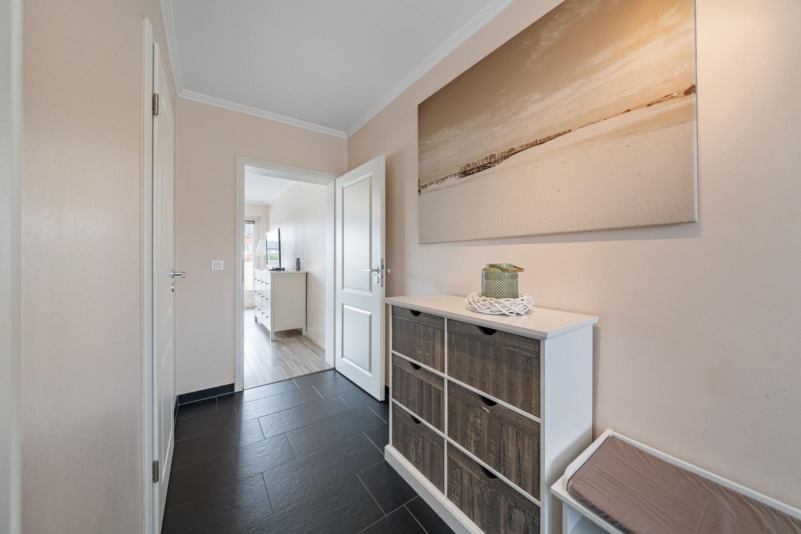 Flur mit Schuhschrank, Wandbild und Tür zu Wohnzimmer.